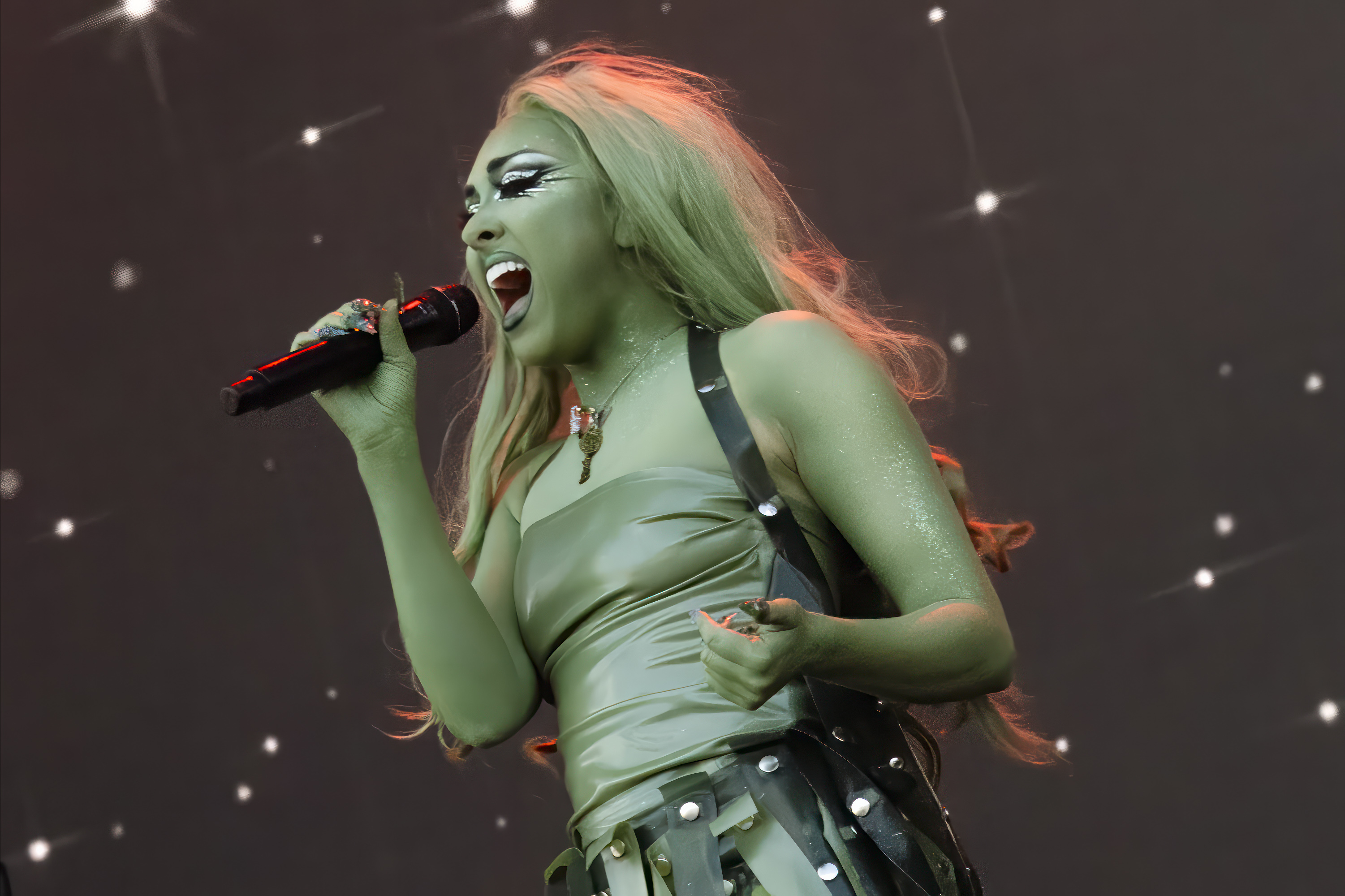 Chappell Roan passionately singing into a microphone on stage, wearing a futuristic, strap-filled outfit