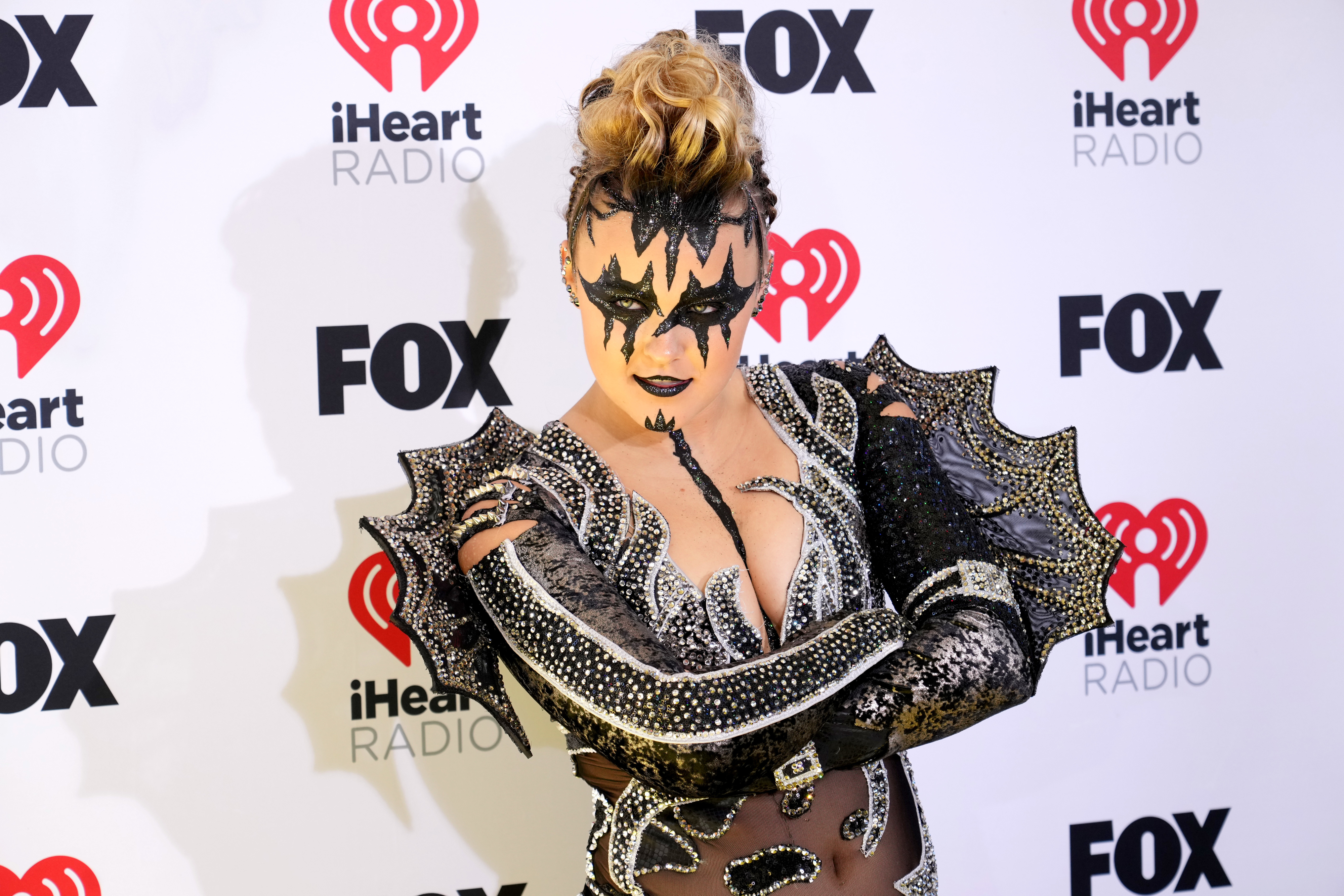 An attendee poses at the iHeartRadio event, wearing a black and metallic costume with wing-like protrusions and dramatic face makeup