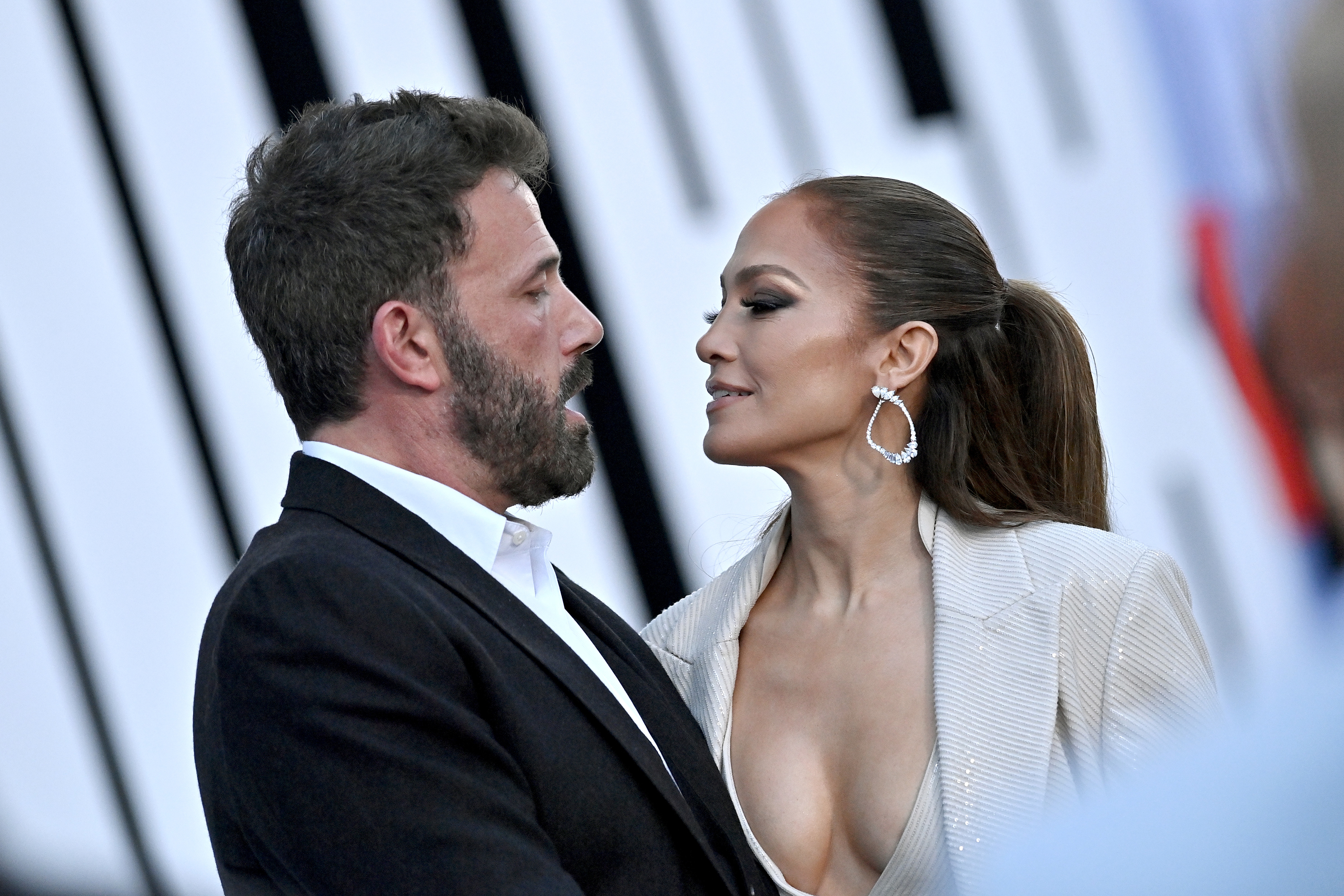 Ben Affleck and Jennifer Lopez share a moment on the red carpet, with Jennifer wearing a stylish outfit featuring a deep neckline and statement earrings