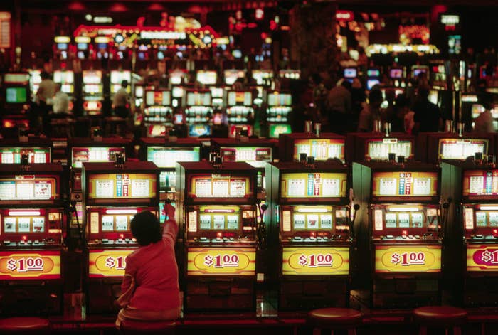 A person in a casino plays a $100 slot machine. Multiple slot machines are visible in the background with a few other patrons