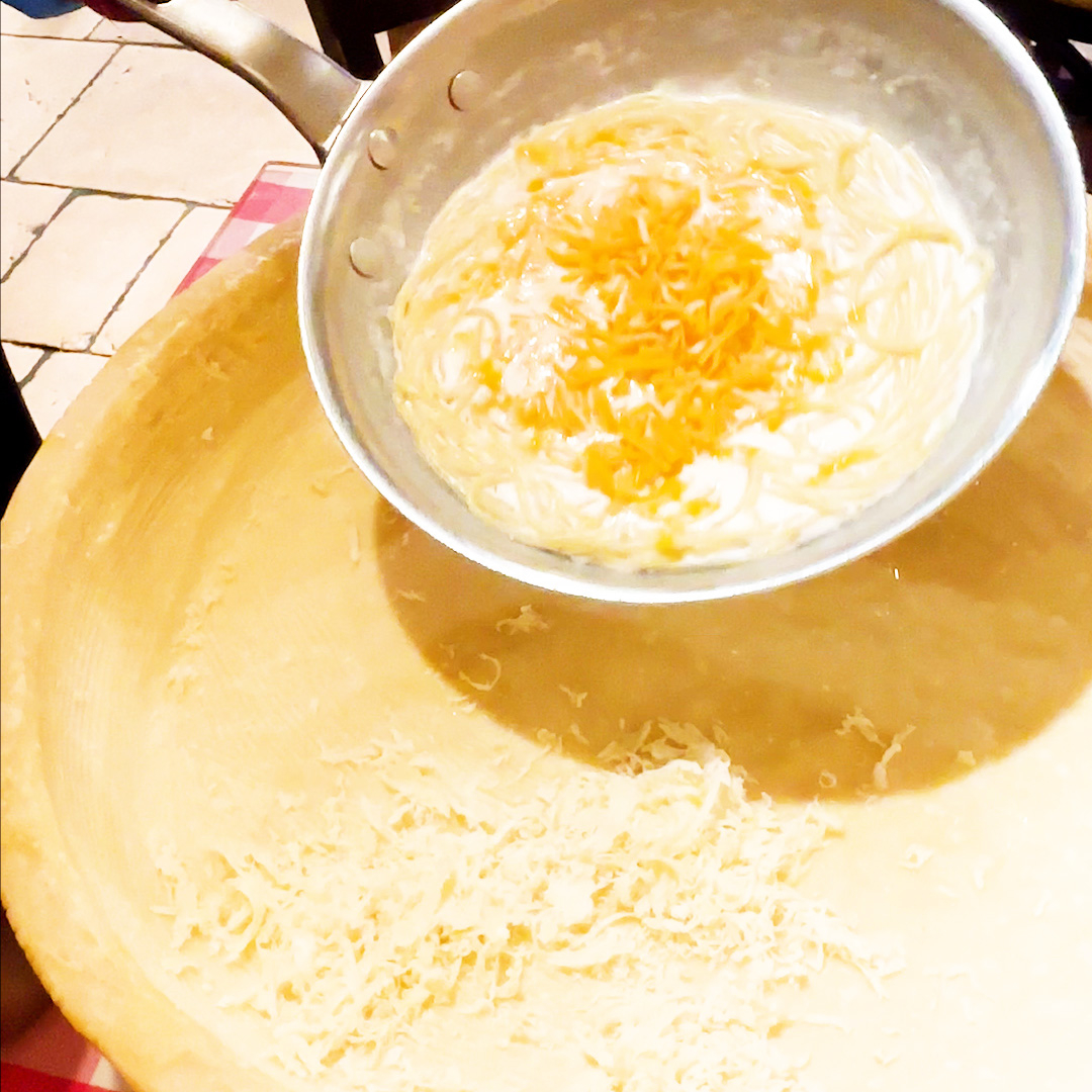 おろしたてのチーズがかかった熱々のパスタが薄焼きの鍋に入っている料理の画像です。