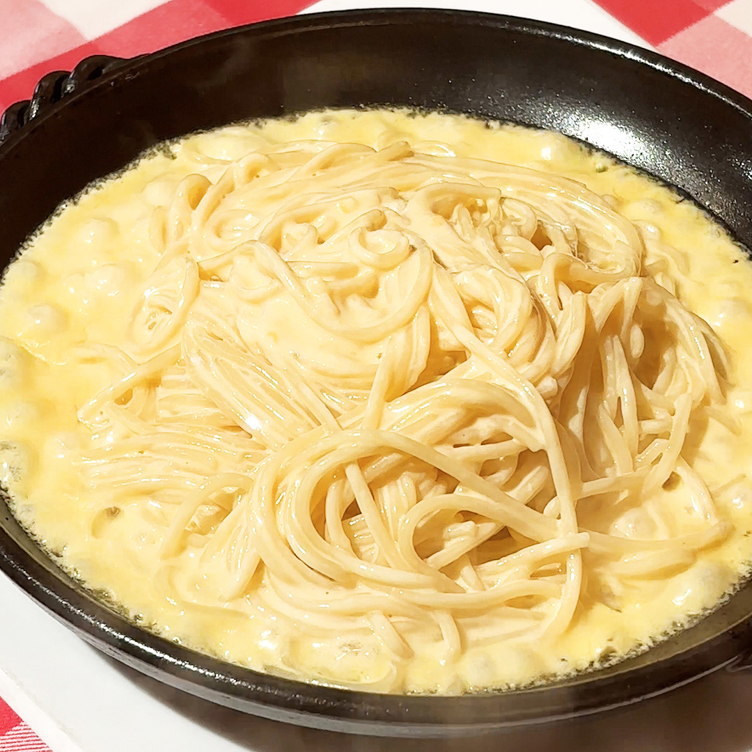 クリーミーなソースがたっぷり絡んだスパゲティが黒い皿に盛られている。背景には赤と白のチェッカーテーブルクロスが見える。