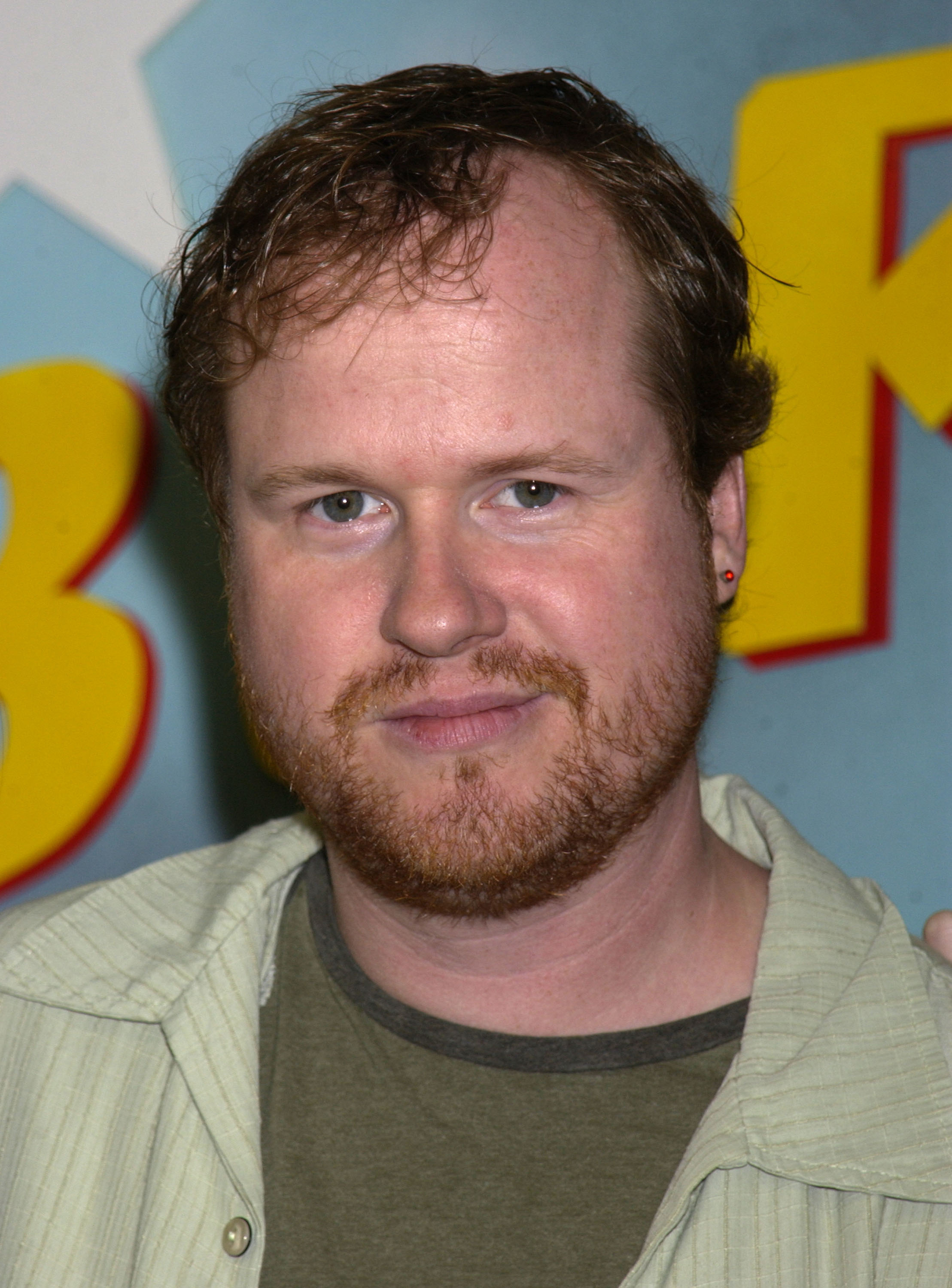 Joss Whedon standing in front of a colorful backdrop with large yellow letters