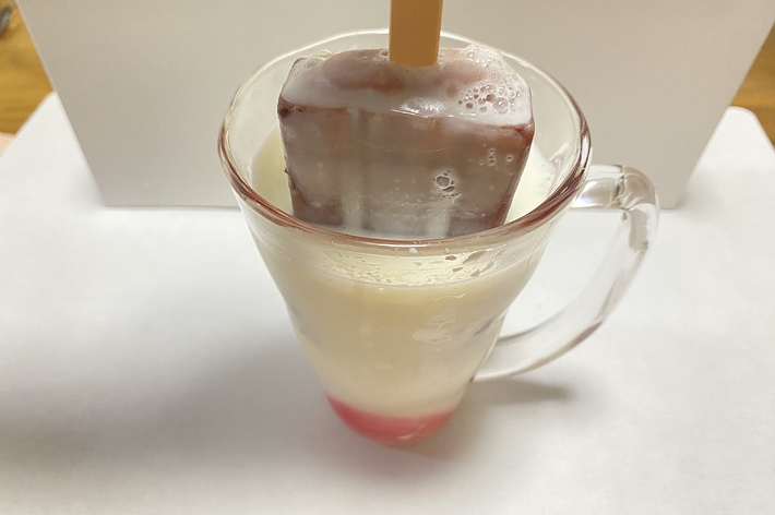 冷たい飲み物の中にアイスキャンディーが入っているガラスのコップ。