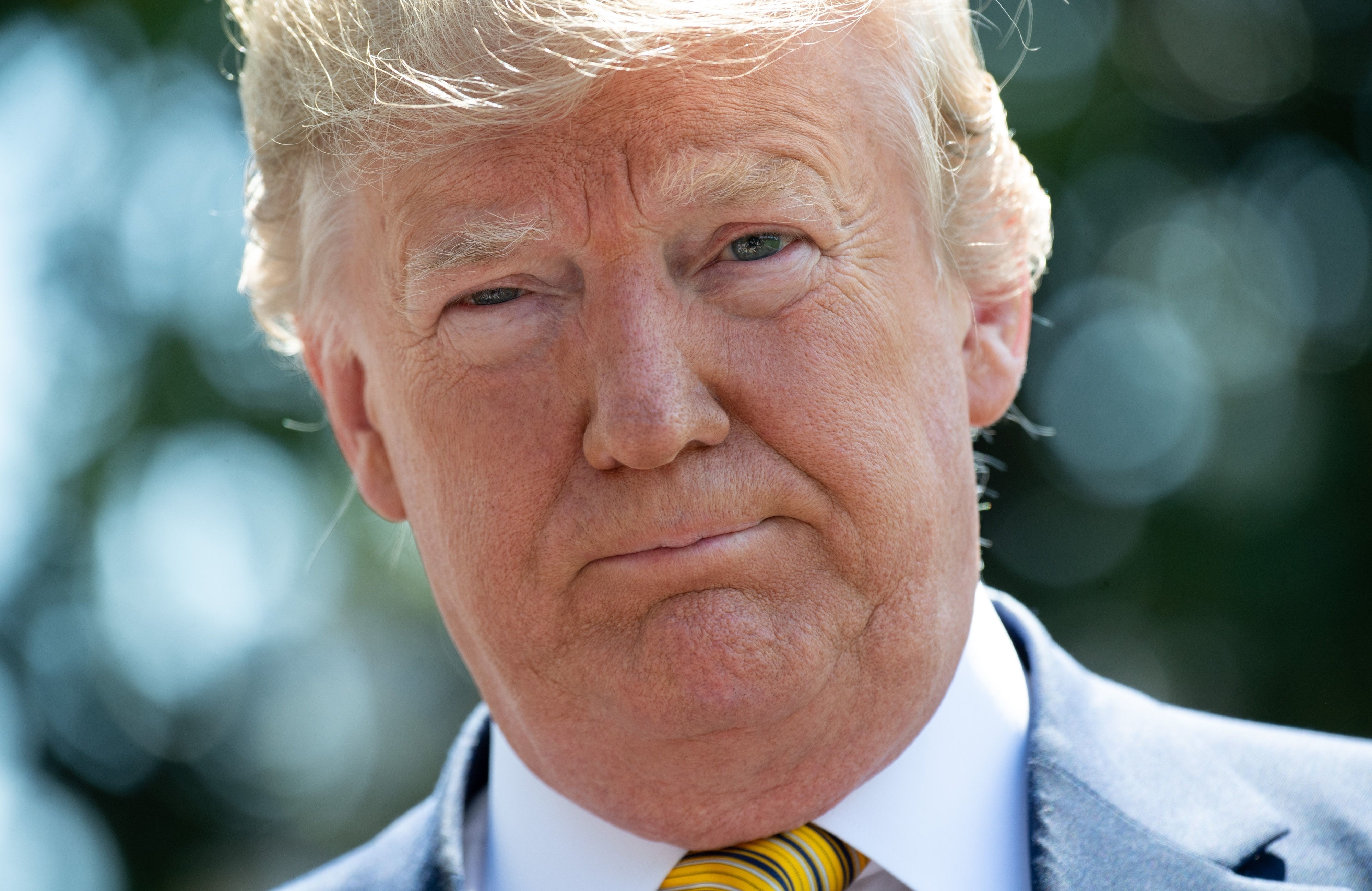 A man in a suit with a yellow tie is looking directly at the camera outdoors