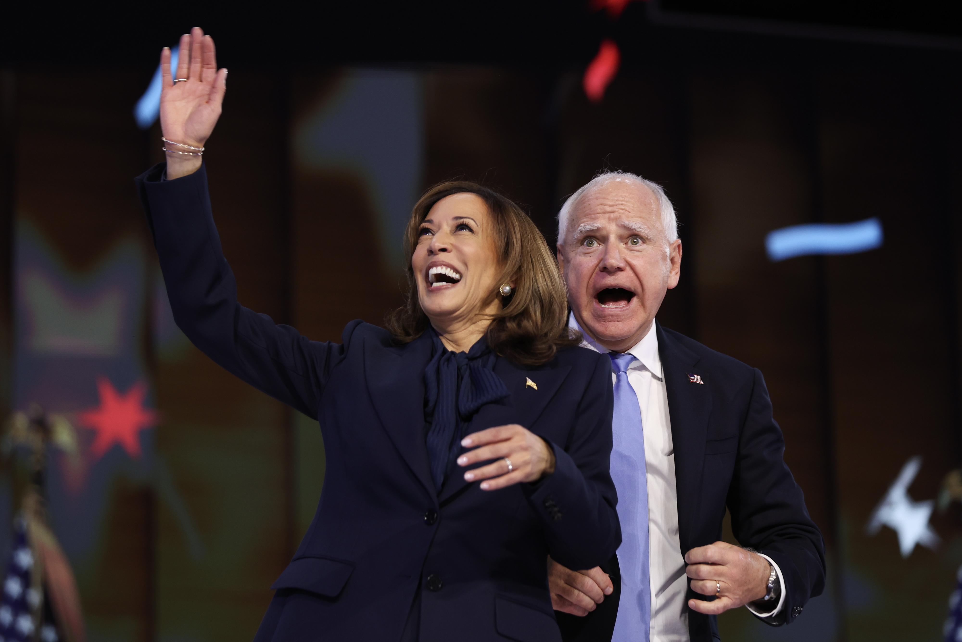 Kamala Harris and Tim Walz smile and wave energetically at an event