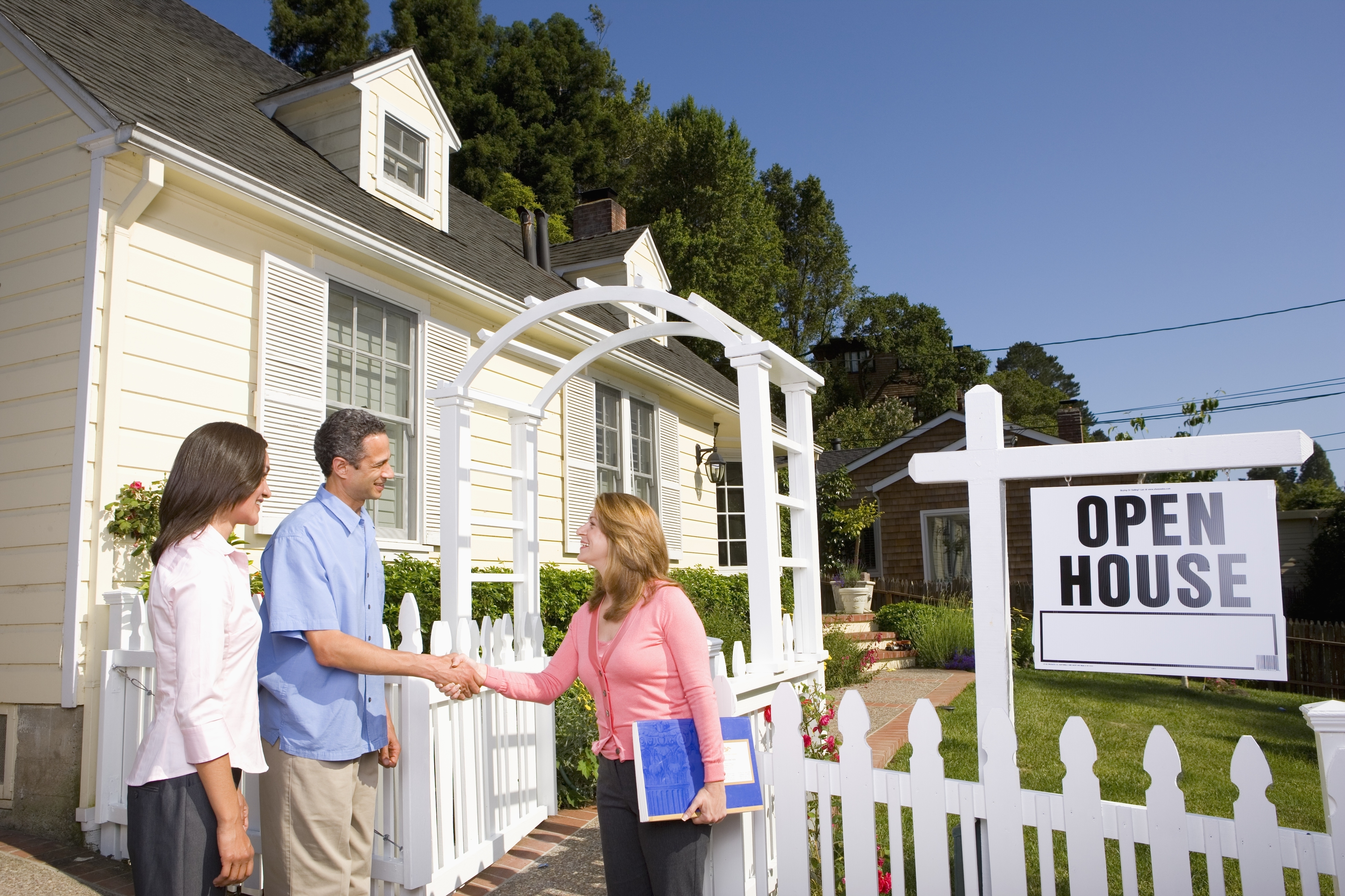 People are standing outside a house with an "Open House" sign. Two individuals are shaking hands while another person looks on