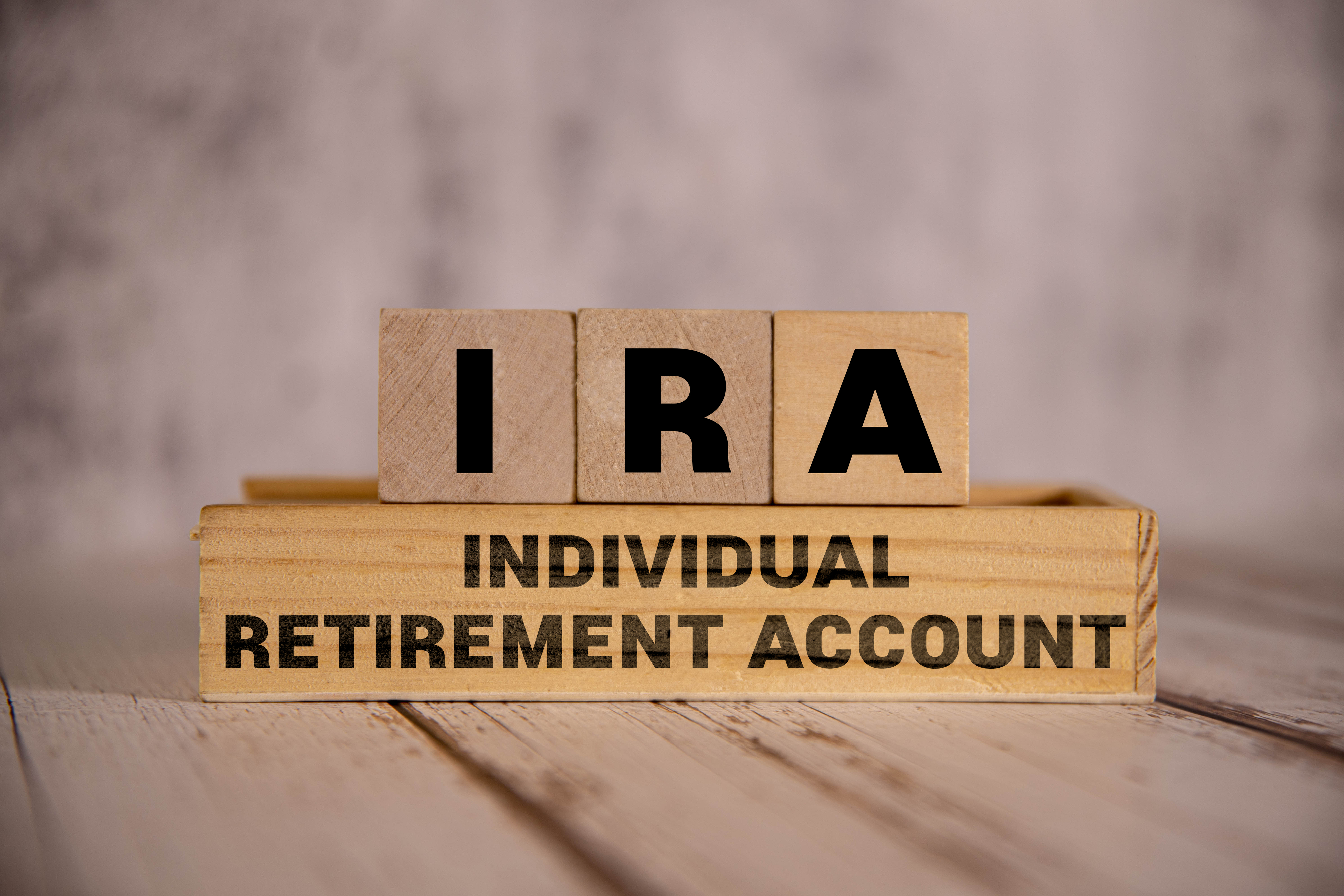 Wooden blocks with the letters "IRA" atop a small wooden shelf labeled "INDIVIDUAL RETIREMENT ACCOUNT."