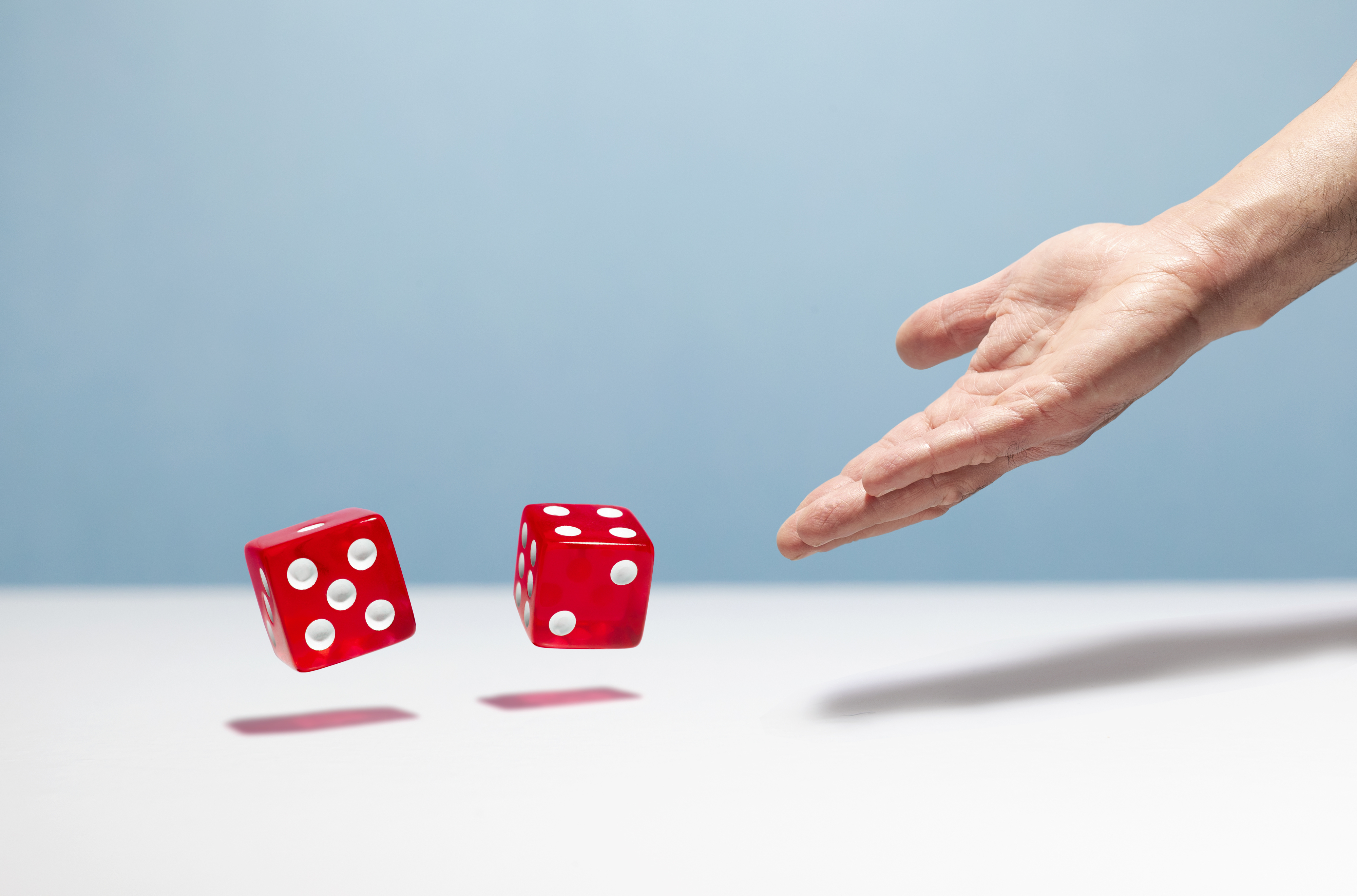 A hand tossing two red dice with white dots against a plain backdrop