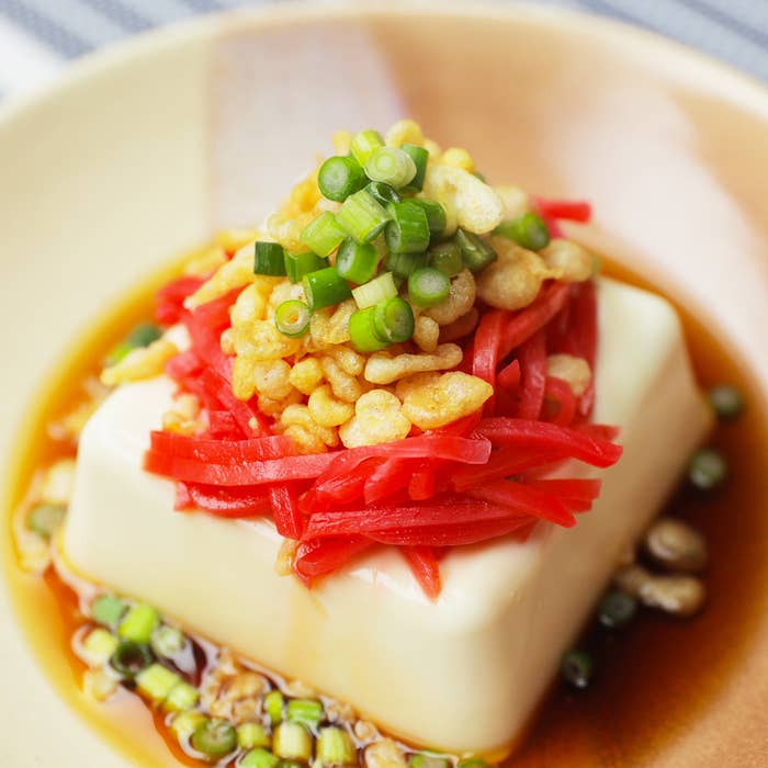 豆腐の前菜が、ソース、細切りの生姜、揚げ物、および刻みネギで飾られている。