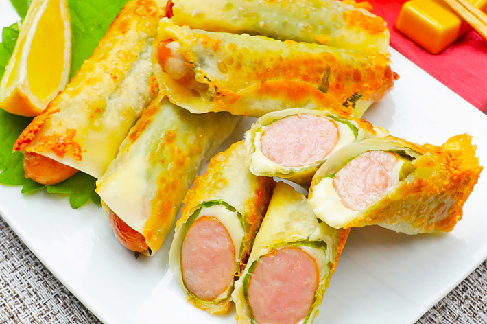 皿に盛られたフライド春巻き、ソーセージとチーズが詰めてある。レモンのスライスとガラスの飲み物が添えられている。