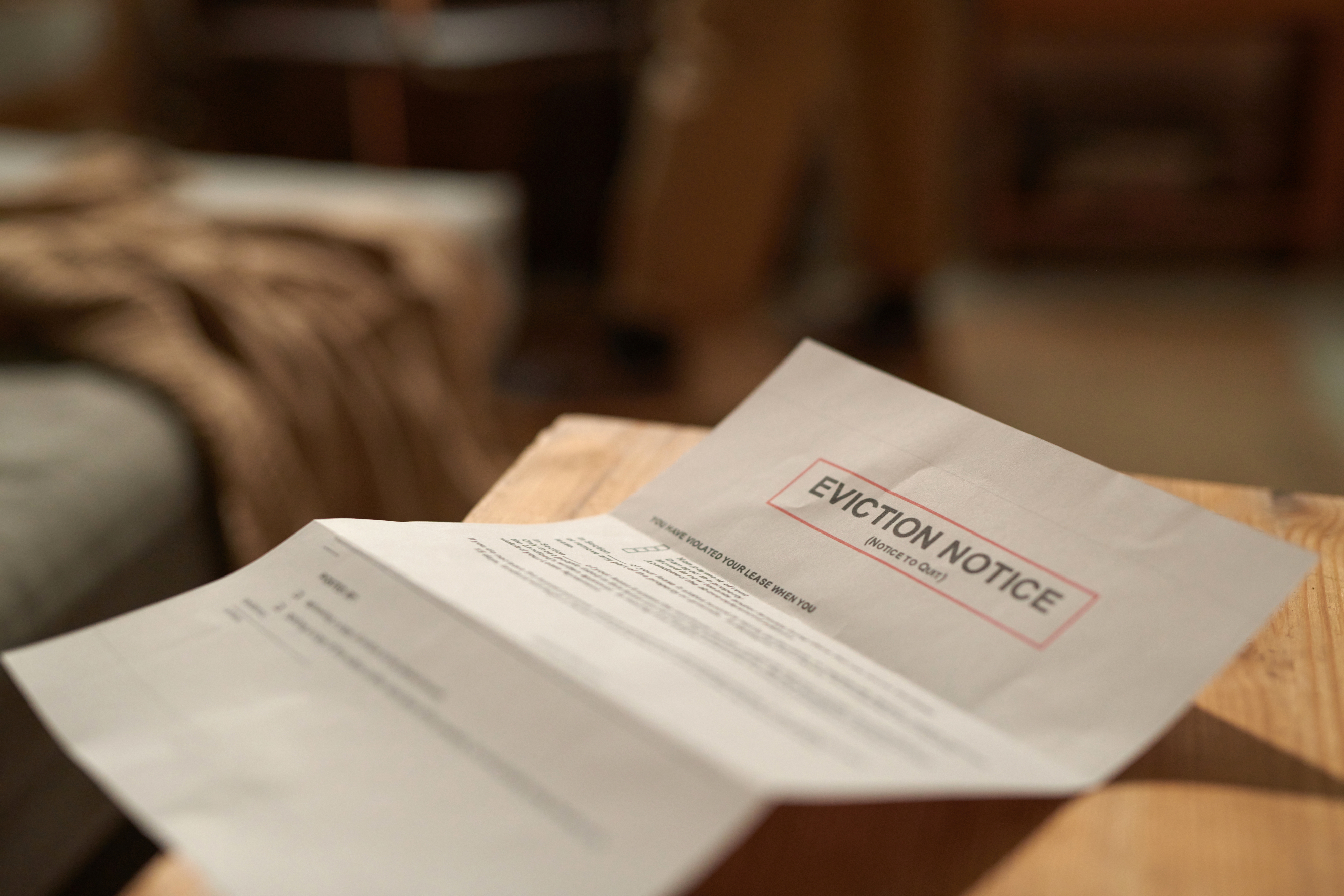 An eviction notice is placed on a wooden surface with blurred background elements. The notice includes a heading and body text detailing eviction information