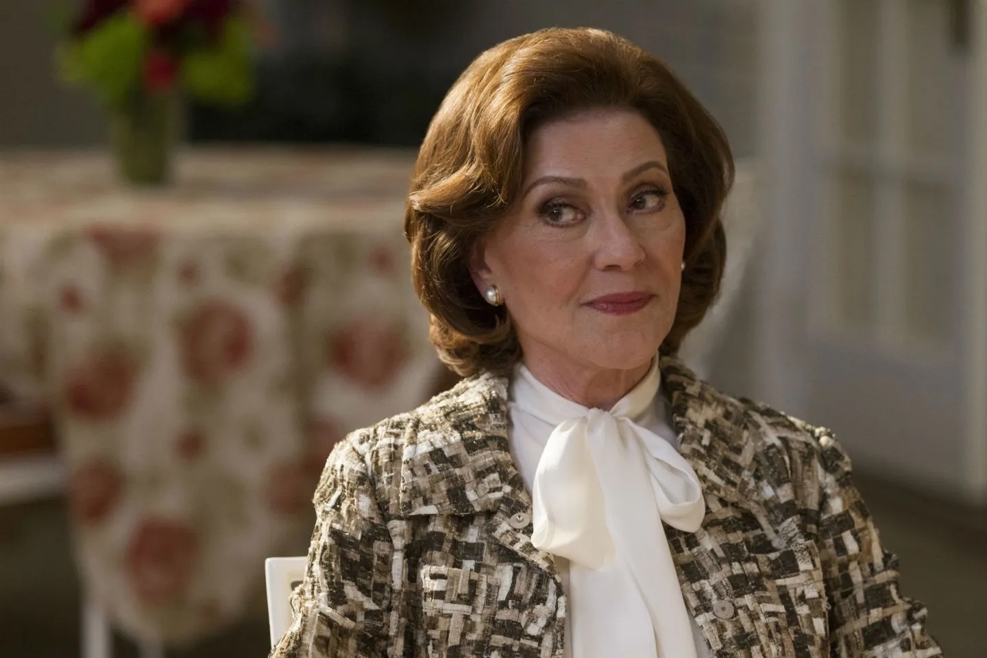 Emily Gilmore from "Gilmore Girls" dressed in a patterned jacket with a white bow blouse, sitting at a table