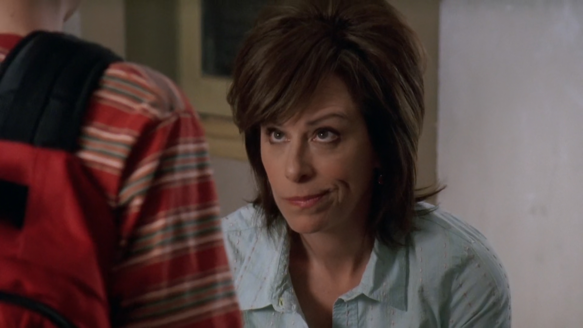 Jane Kaczmarek looks up while talking to someone wearing a striped shirt and a backpack in a scene from a TV show