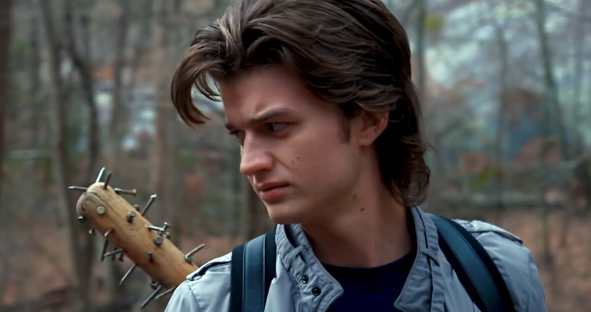Joe Keery as Steve Harrington in a forest scene from "Stranger Things," holding a spiked baseball bat over his shoulder