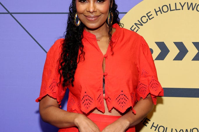 Sanaa Lathan smiles at an event, wearing a stylish two-piece outfit with a patterned top and matching skirt