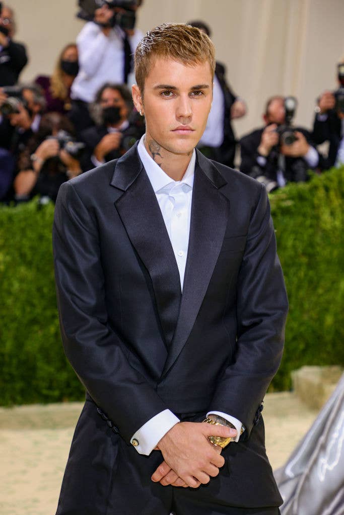 Justin Bieber in a tailored suit poses for photographs on the red carpet. Photographers and media members are in the background