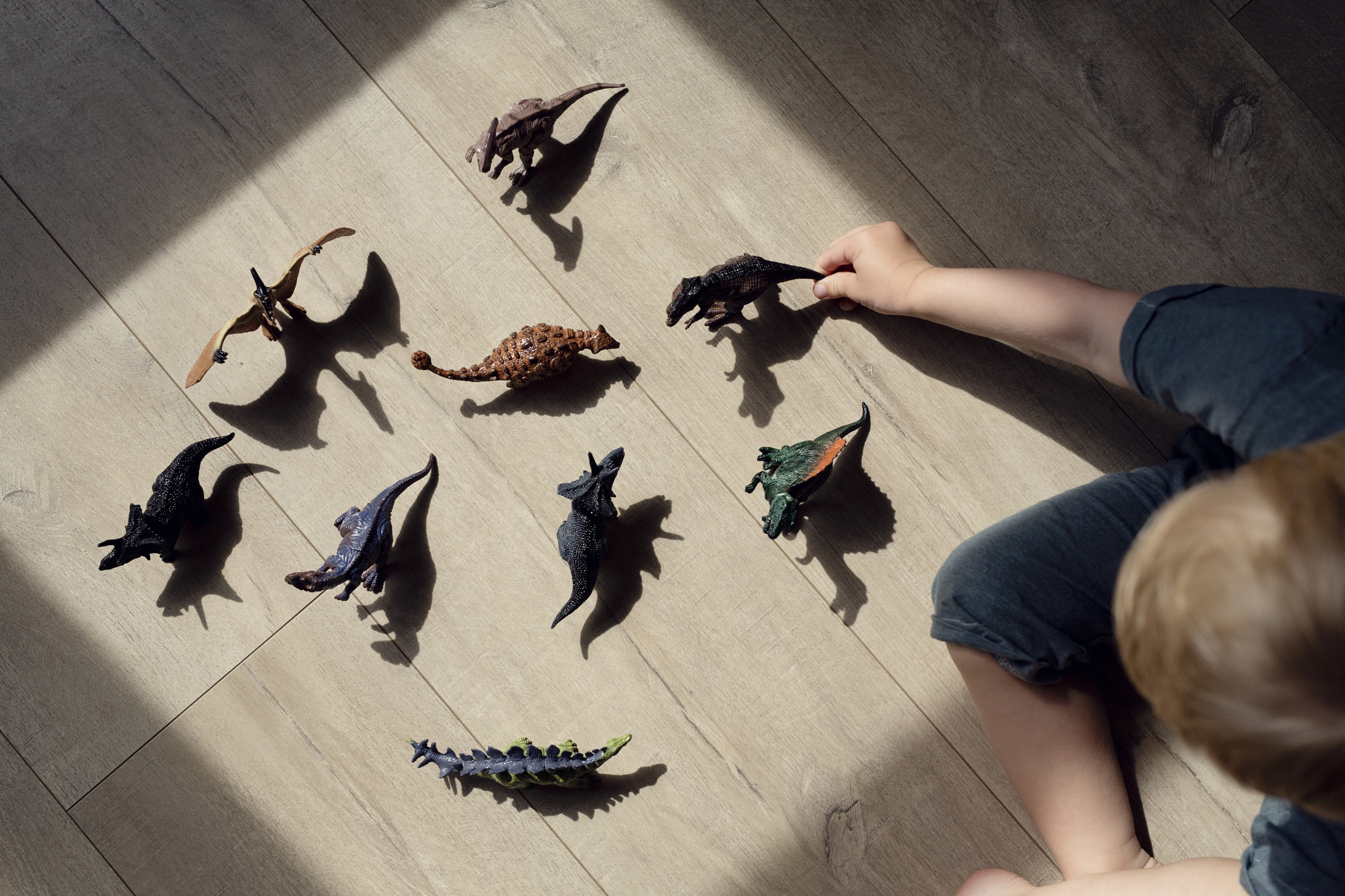 A child is playing on the floor with an arranged collection of dinosaur toys