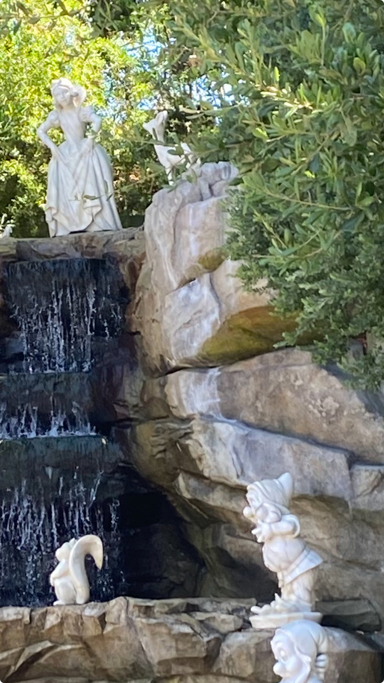 Stone statues of Snow White and the Seven Dwarfs displayed on a rock waterfall feature in a garden setting