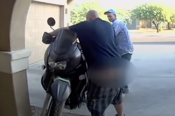 2人の男性がバイクをガレージに押し込んでいる。名前は不明。