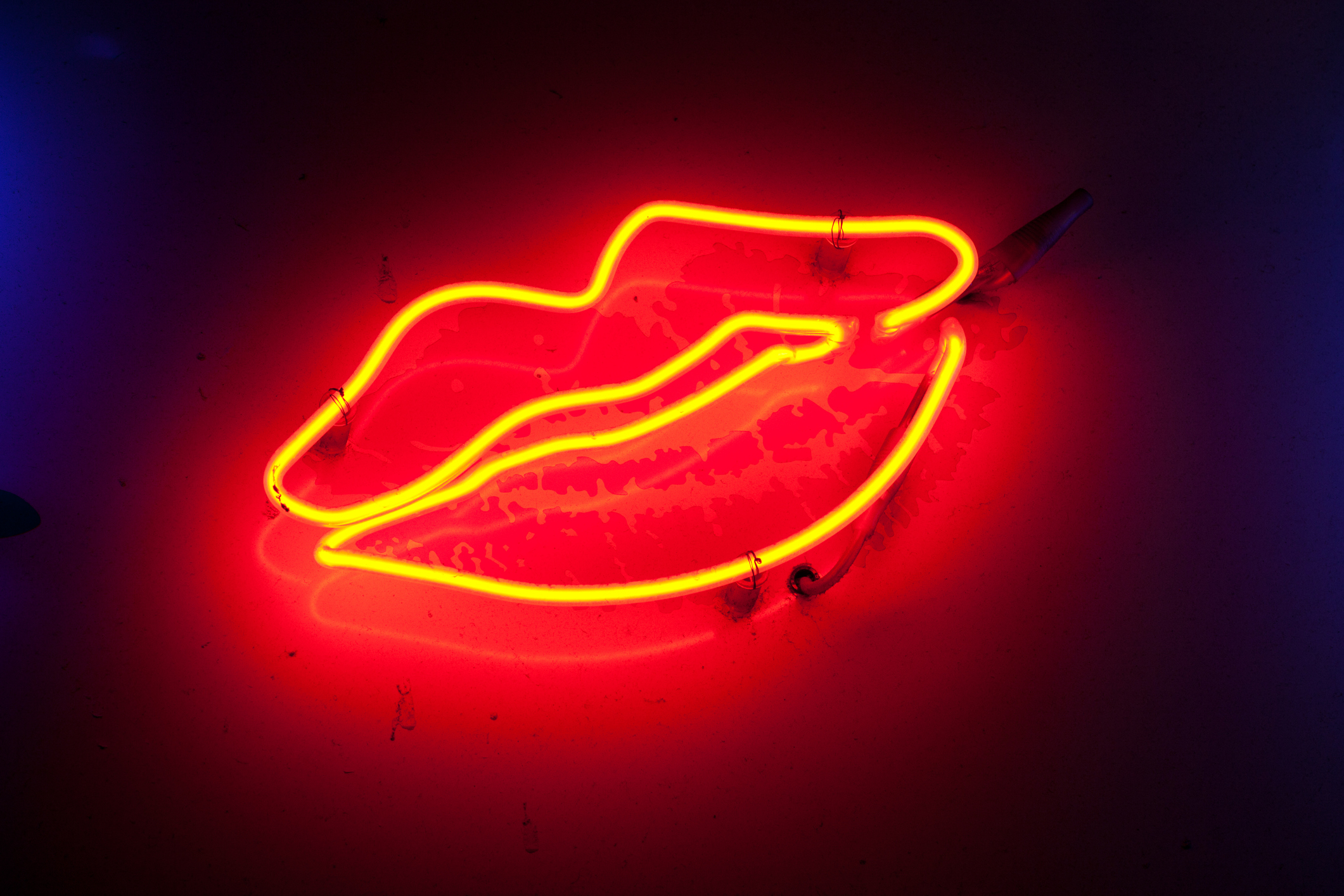 Neon sign in the shape of a pair of lips, glowing in a vibrant red color on a dark background