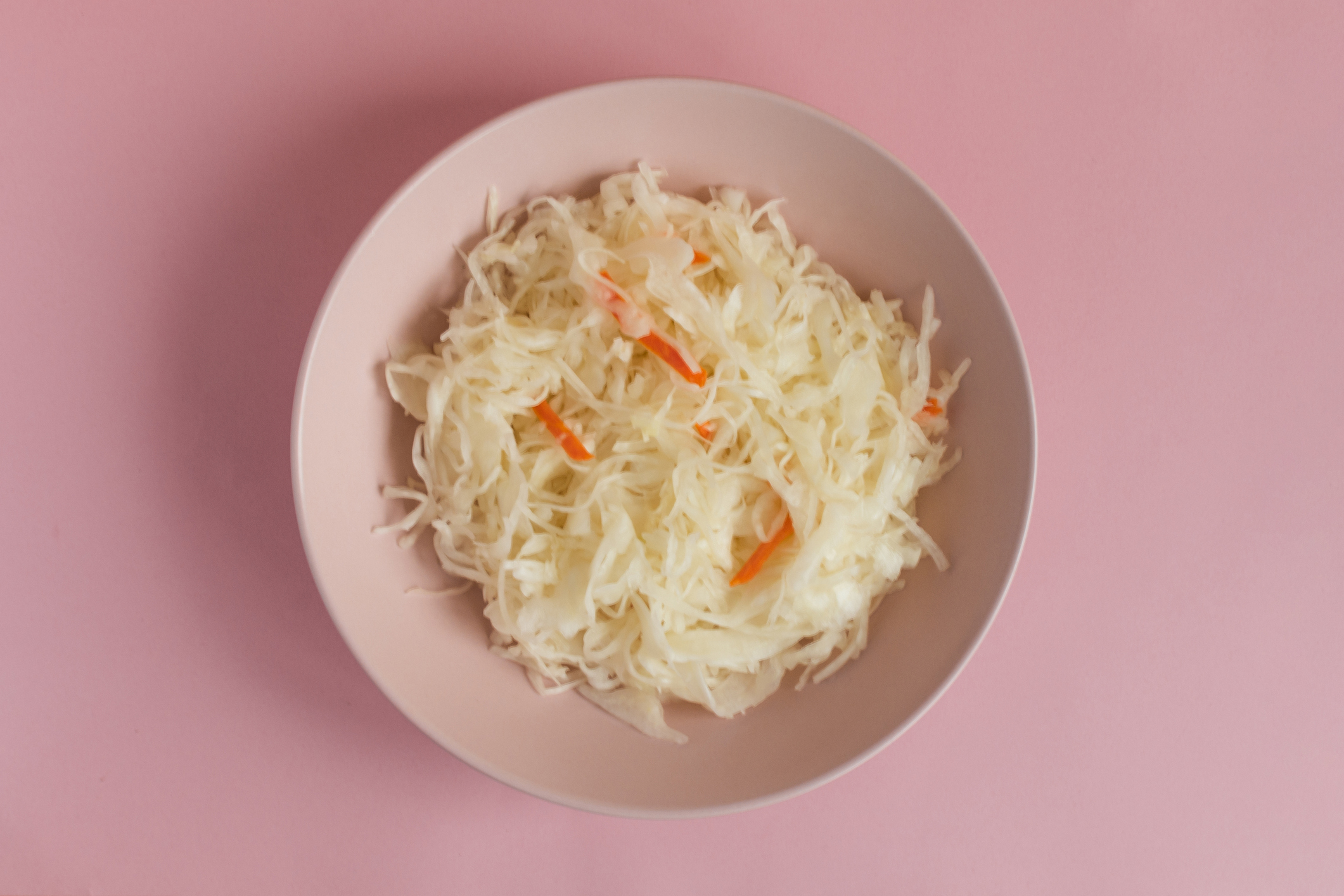 A bowl of coleslaw with shredded cabbage and thin carrot strips, placed against a plain background