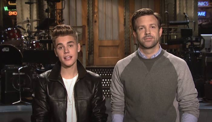 Justin Bieber and Jason Sudeikis stand together on the set of NBC, with musical instruments and equipment visible in the background