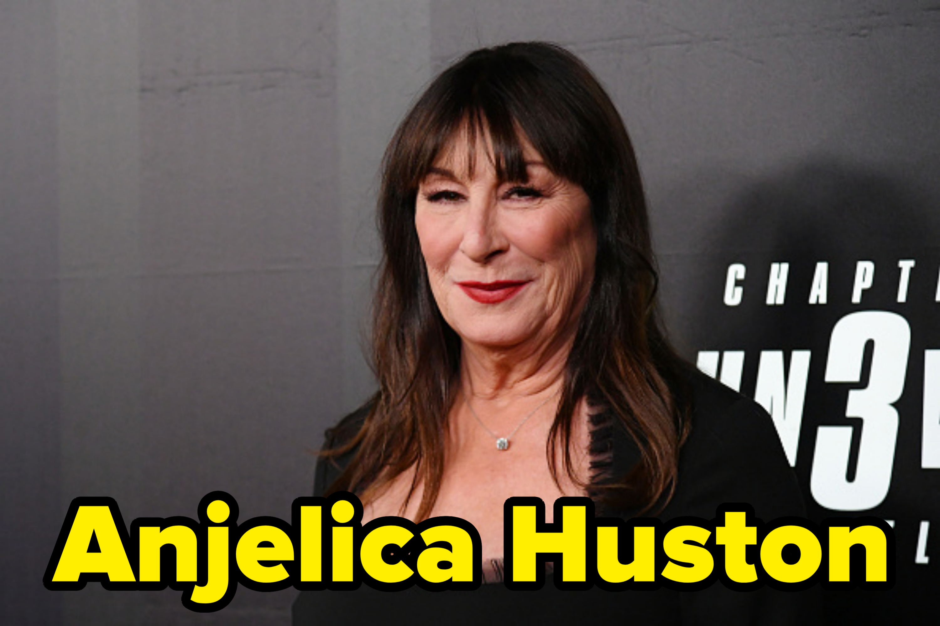 Anjelica Huston in a black dress, smiles on the red carpet at an event for "John Wick: Chapter 3 – Parabellum"