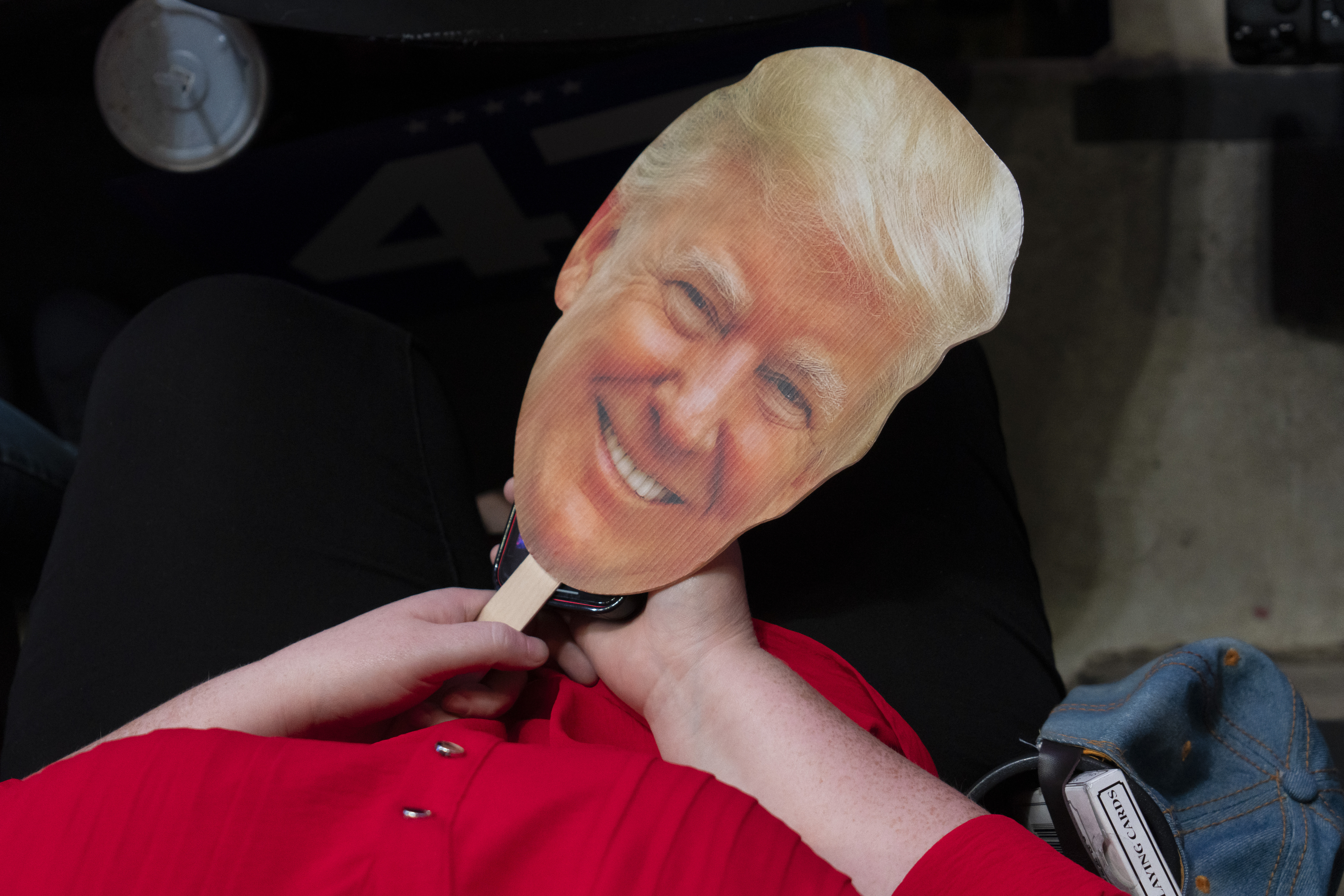 A person holds a large cutout of Donald Trump's face on a stick
