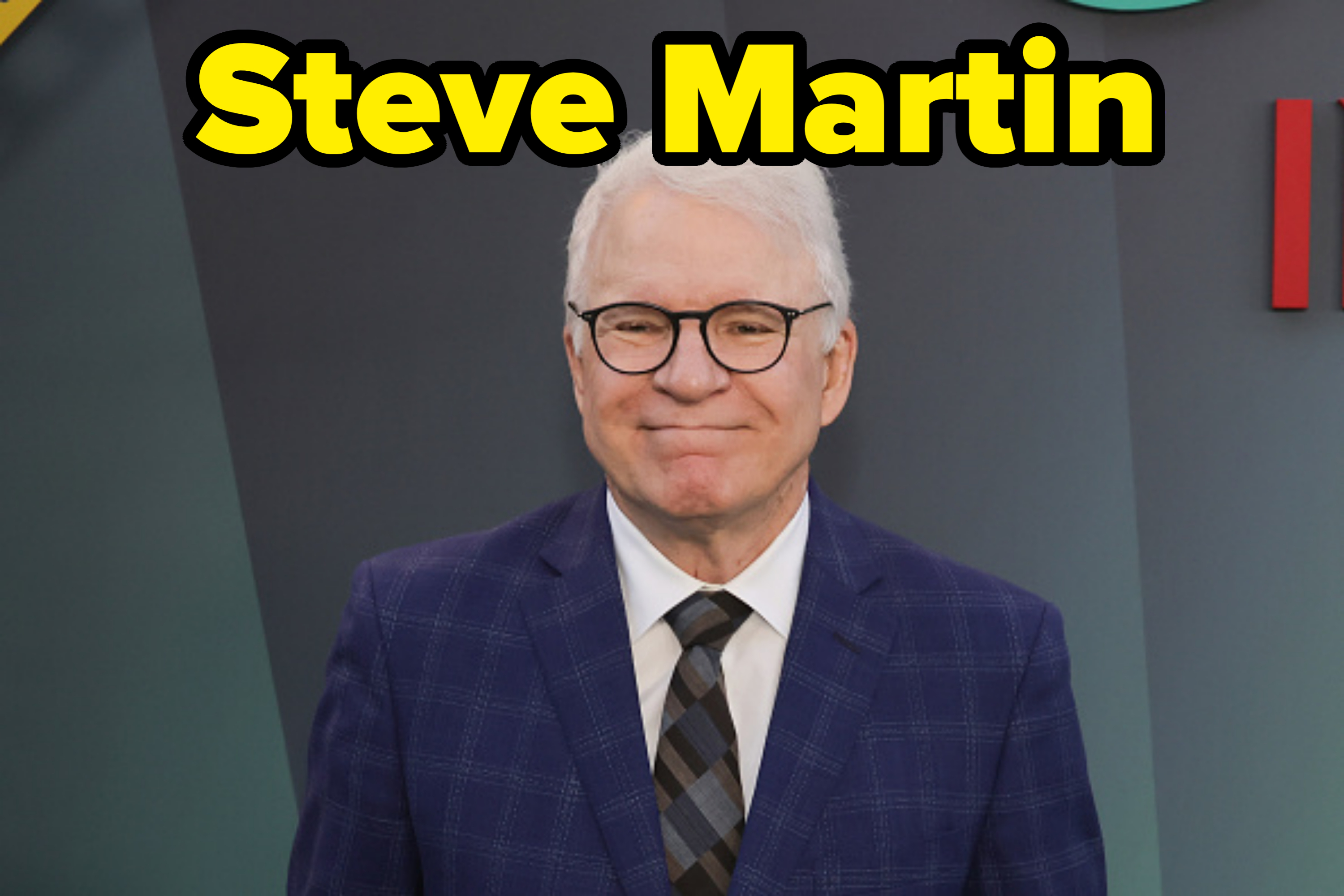 Steve Martin smiles while wearing a checkered suit and a striped tie