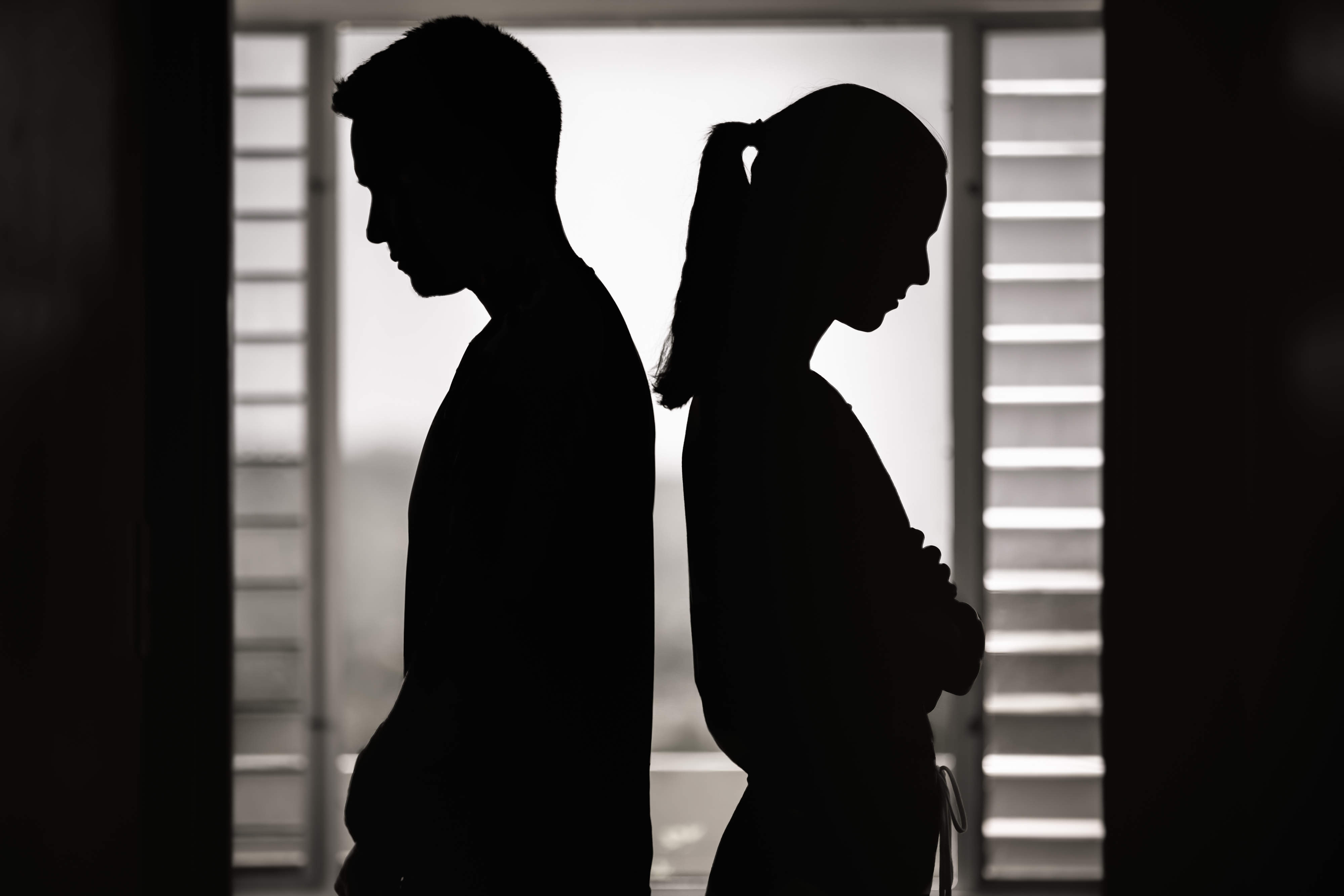 Silhouettes of a man and woman standing back-to-back, looking down, appearing in a contemplative or reflective mood