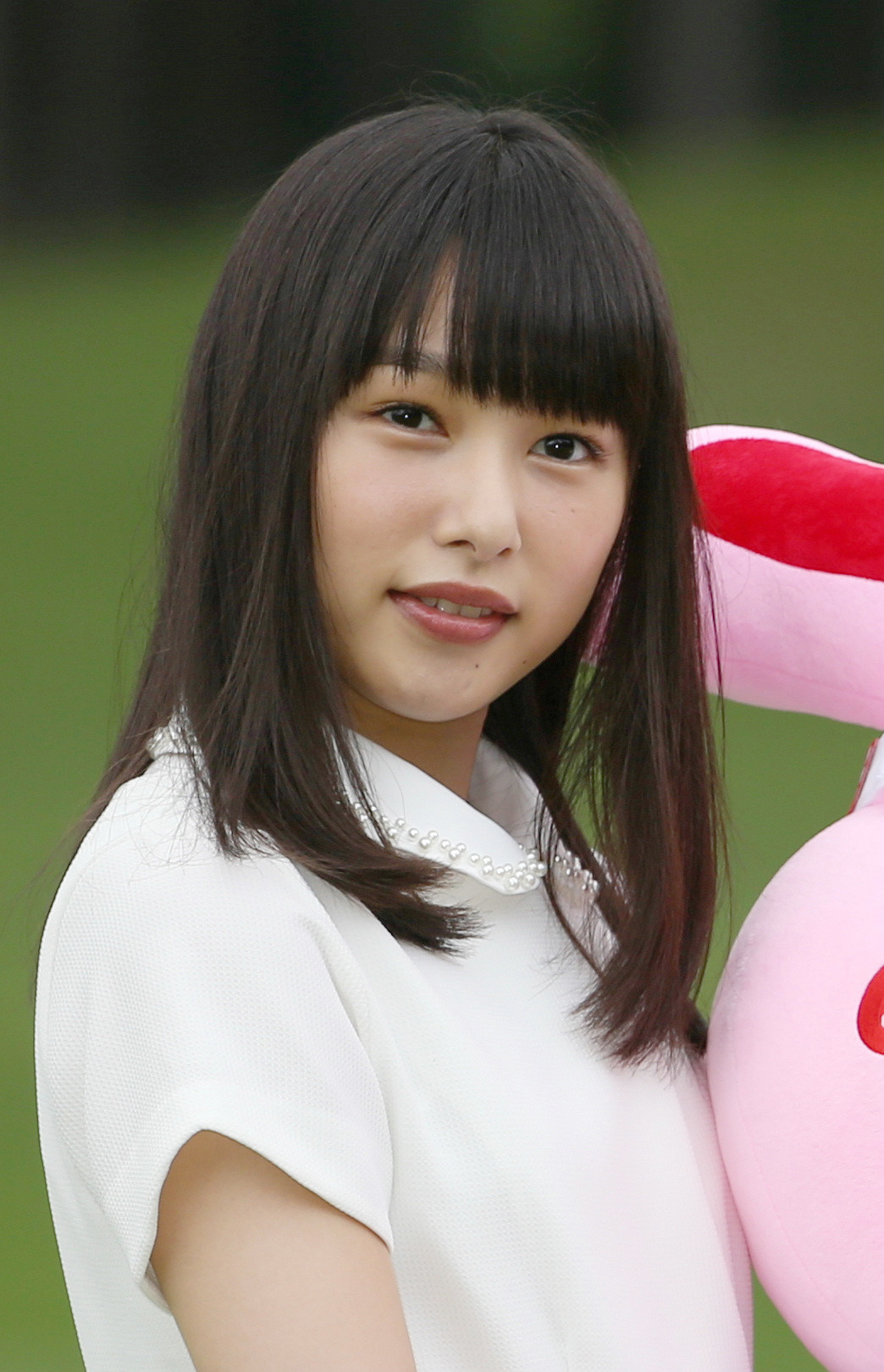 女性が白い服を着て、大きなピンクのぬいぐるみを抱えて微笑んでいる。