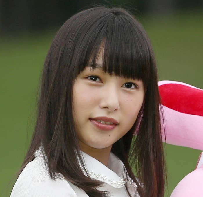 女性が白い服を着て、大きなピンクのぬいぐるみを抱えて微笑んでいる。