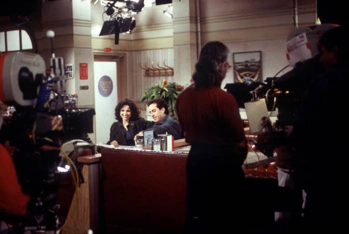Julia Louis-Dreyfus and Jerry Seinfeld film a scene on the set of "Seinfeld" surrounded by production crew and equipment