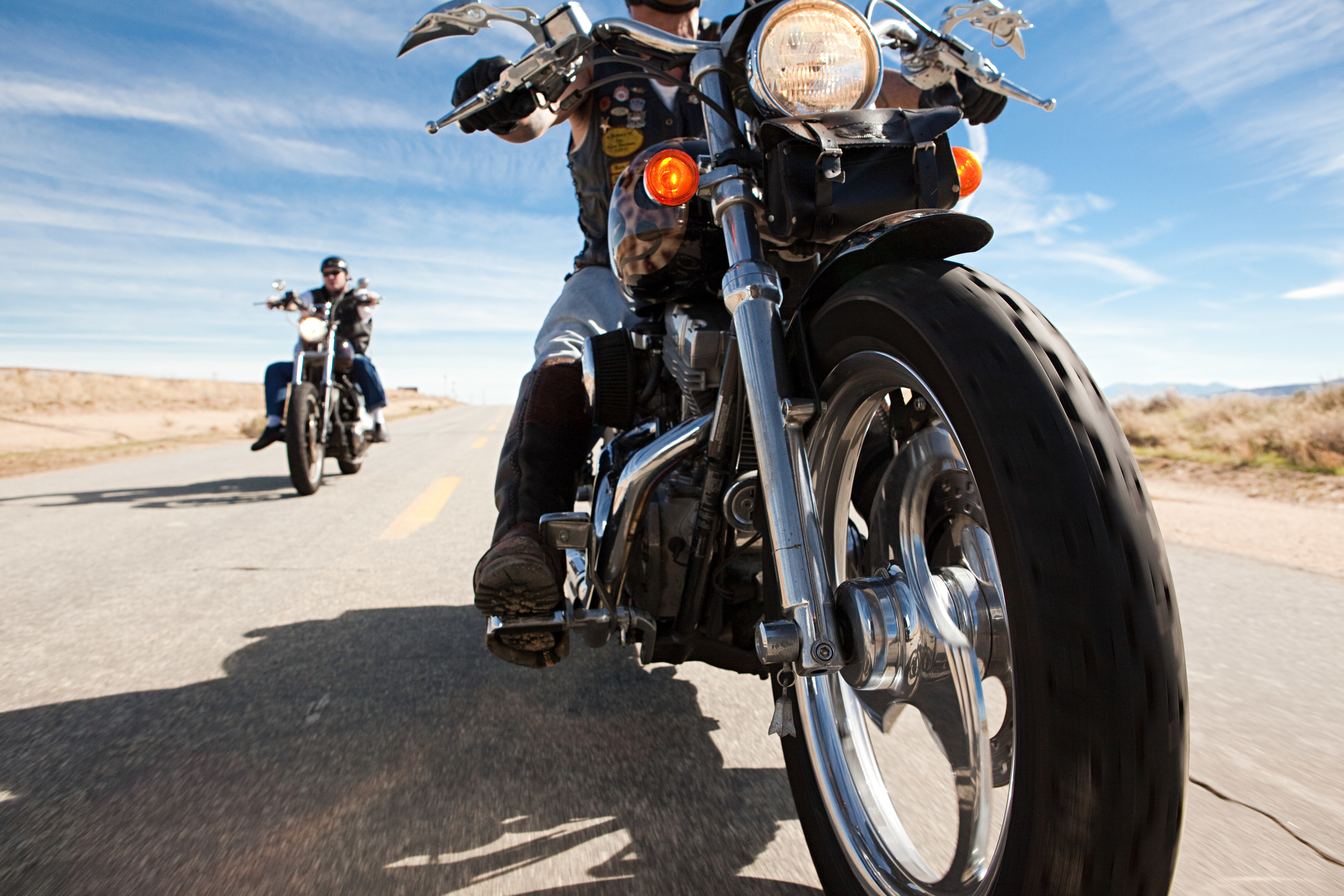 Two motorcyclists ride on an open road in a desert landscape