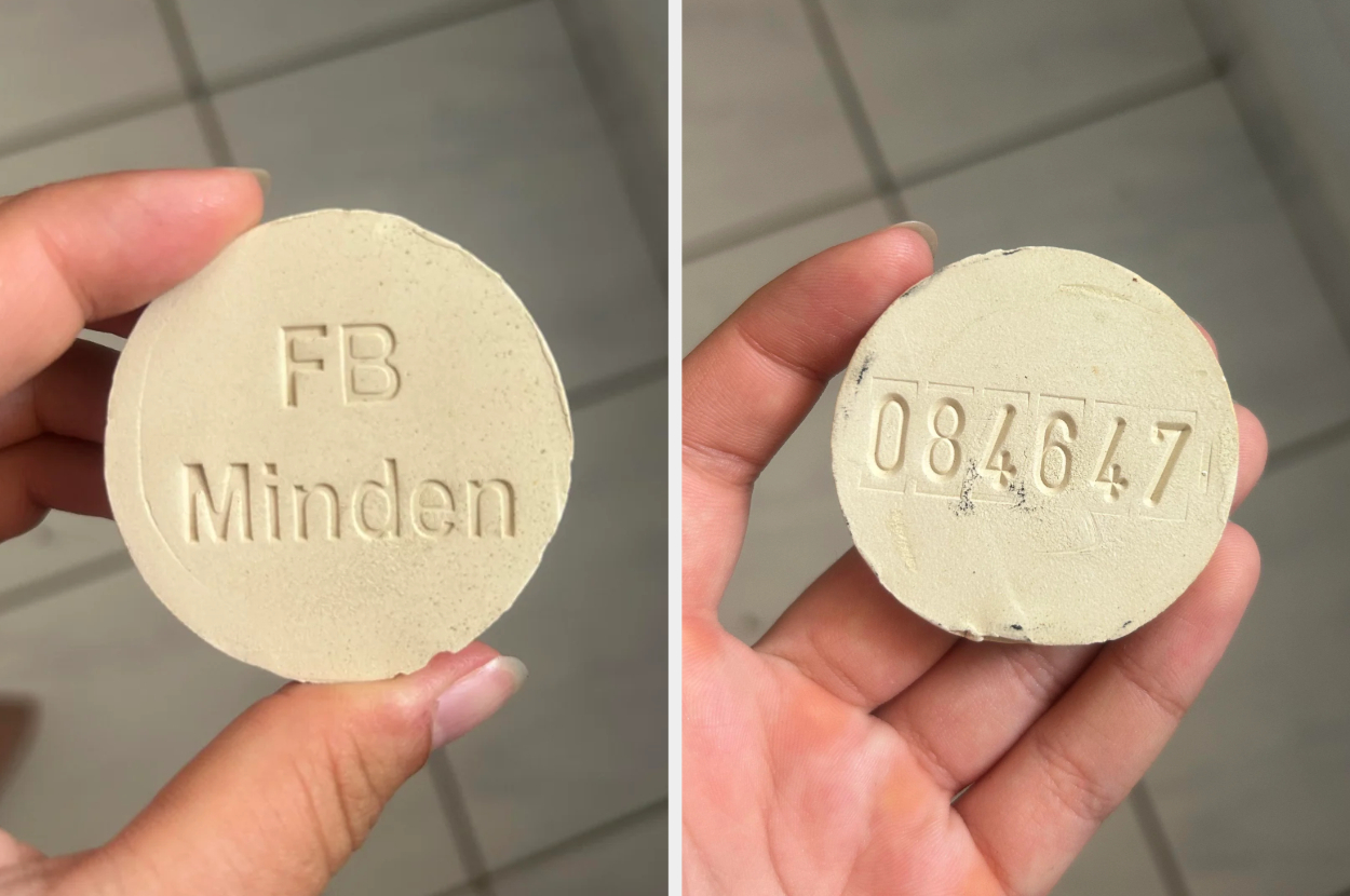 A hand holds a round object with "FB Minden" on one side and "084647" on the opposite side