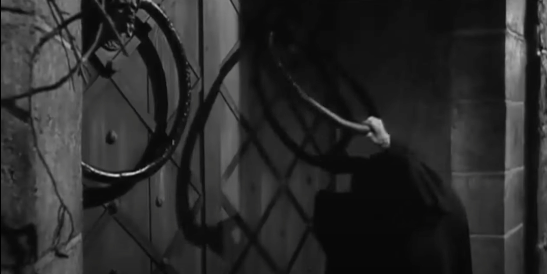 From Young Frankenstein: A hand holding a door knocker in a dark, eerie setting with vines on the door