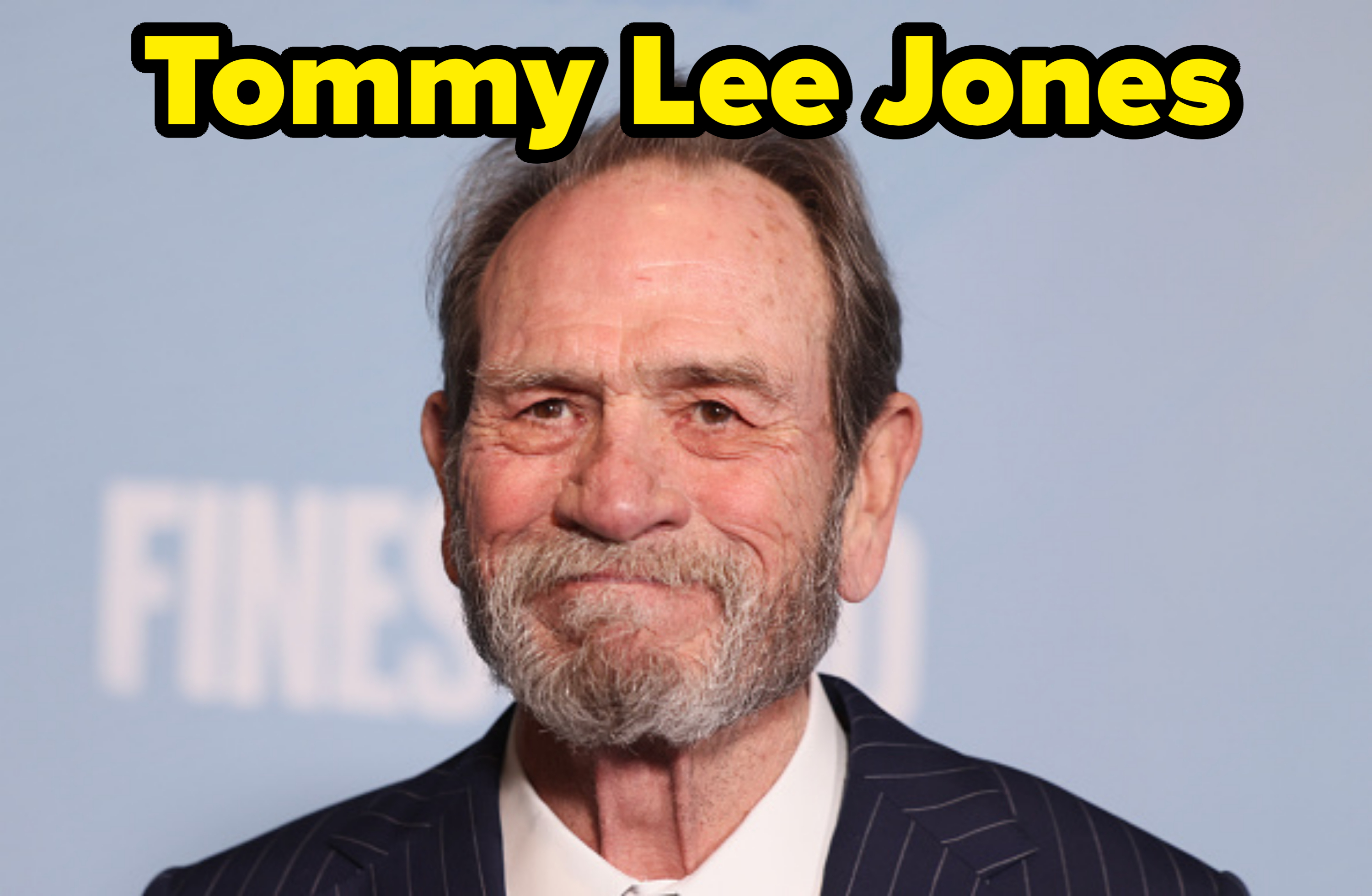 Tommy Lee Jones smiling, wearing a pinstriped suit and white shirt, against a simple background