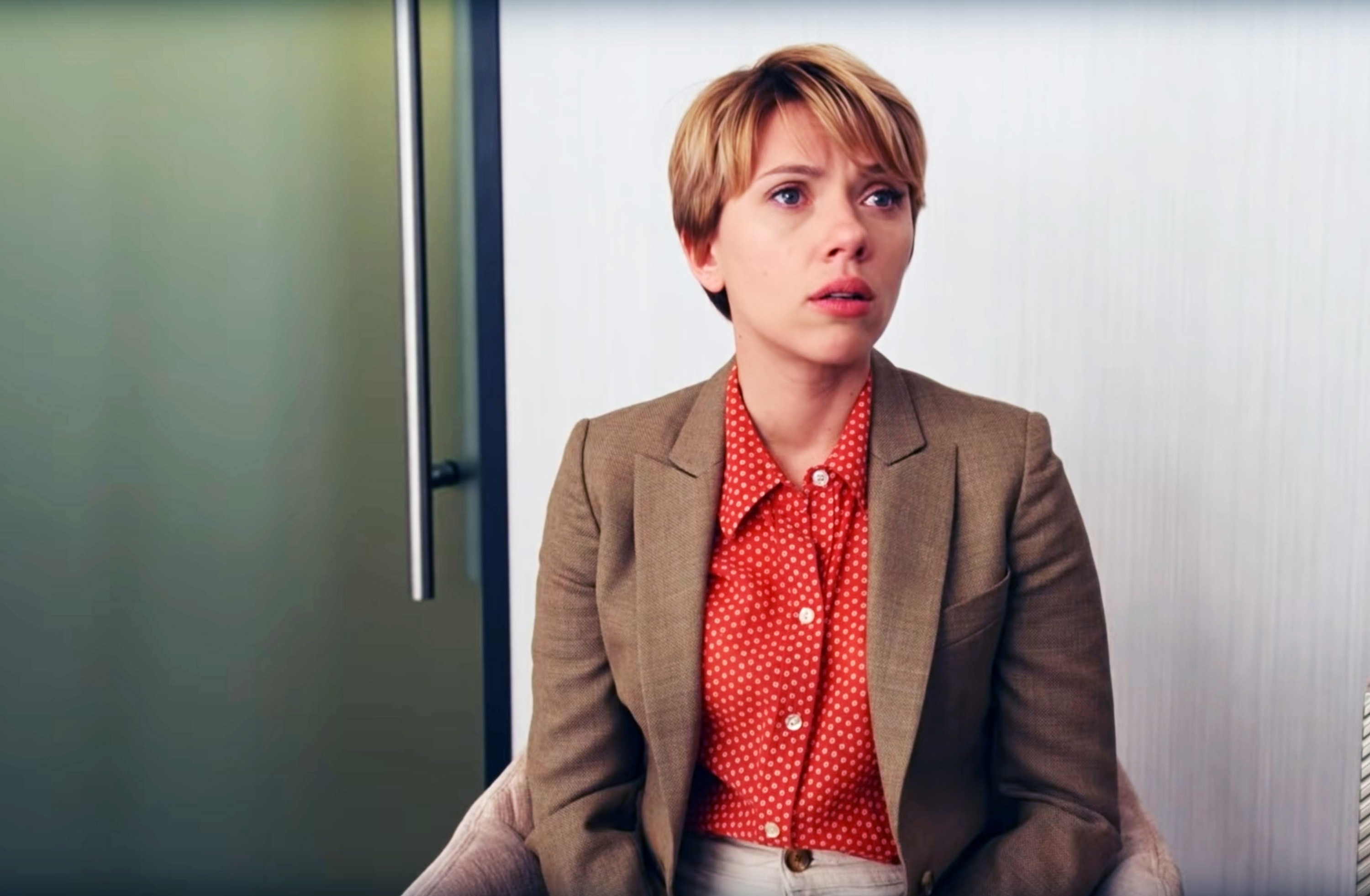 Scarlett Johansson appears concerned while seated indoors, wearing a tan blazer over a red polka dot blouse in "Marriage Story"