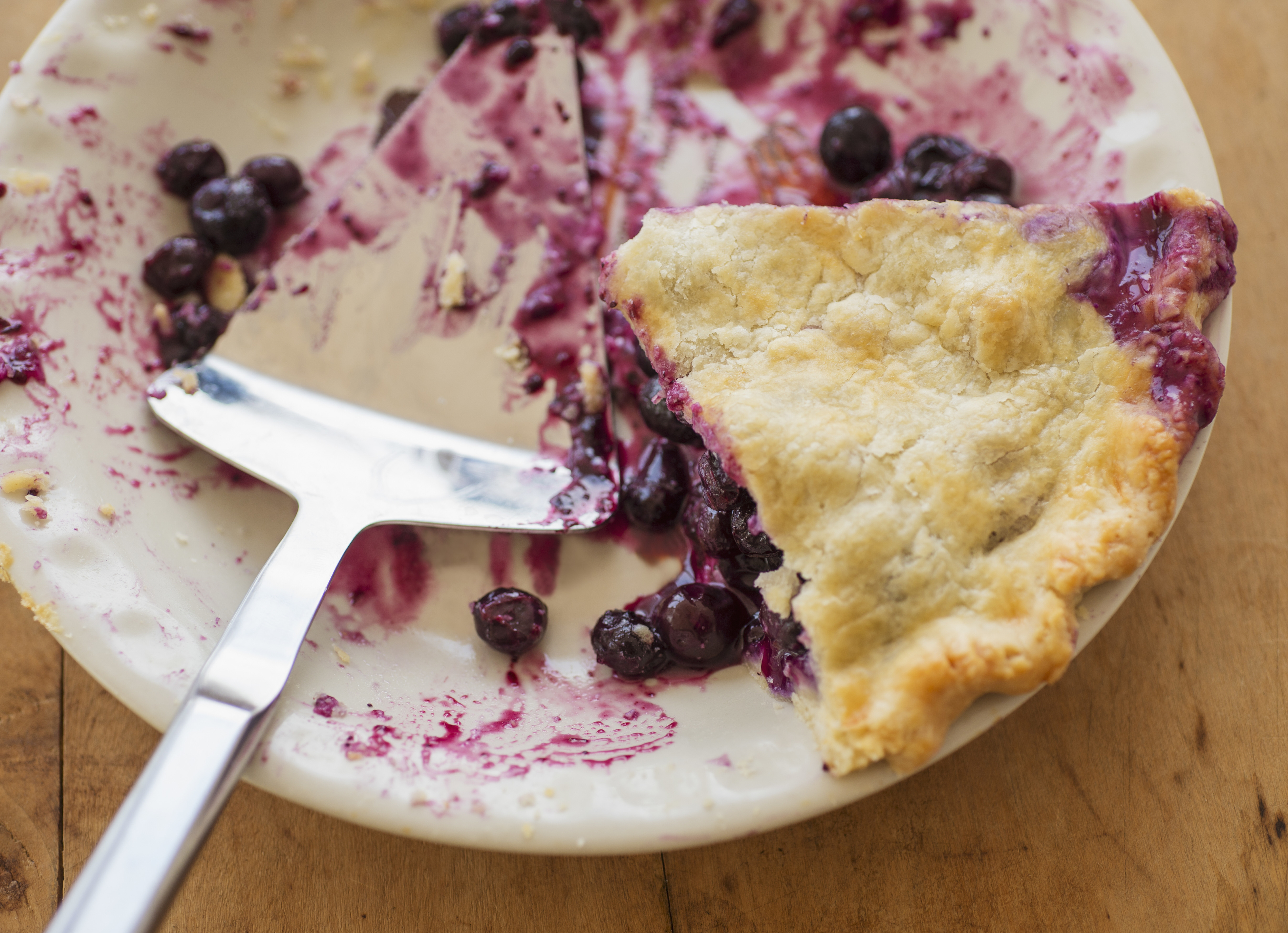 A partially eaten blueberry pie with a serving utensil on a plate, showcasing the remaining slice and scattered blueberries