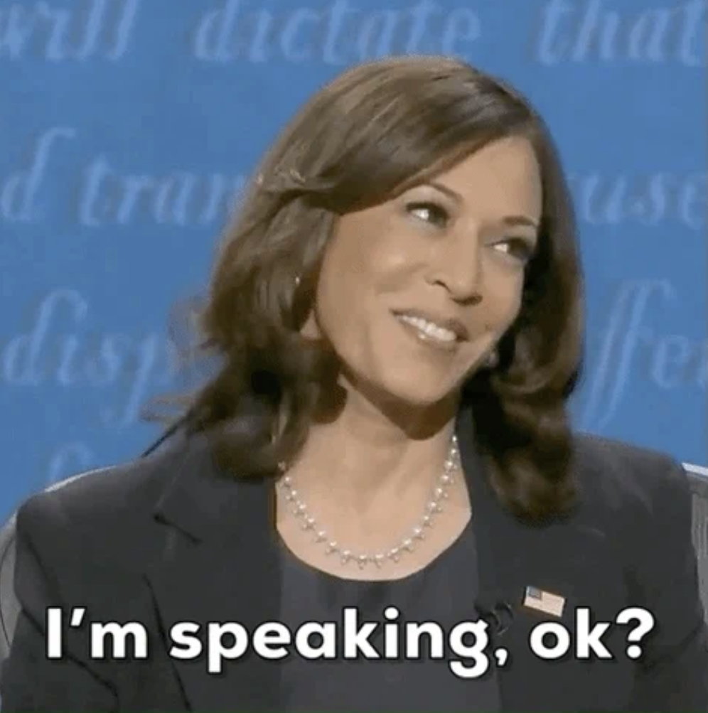 Kamala Harris on a debate stage, smiling and dressed in a business suit, with the text "I'm speaking, ok?" visible at the bottom
