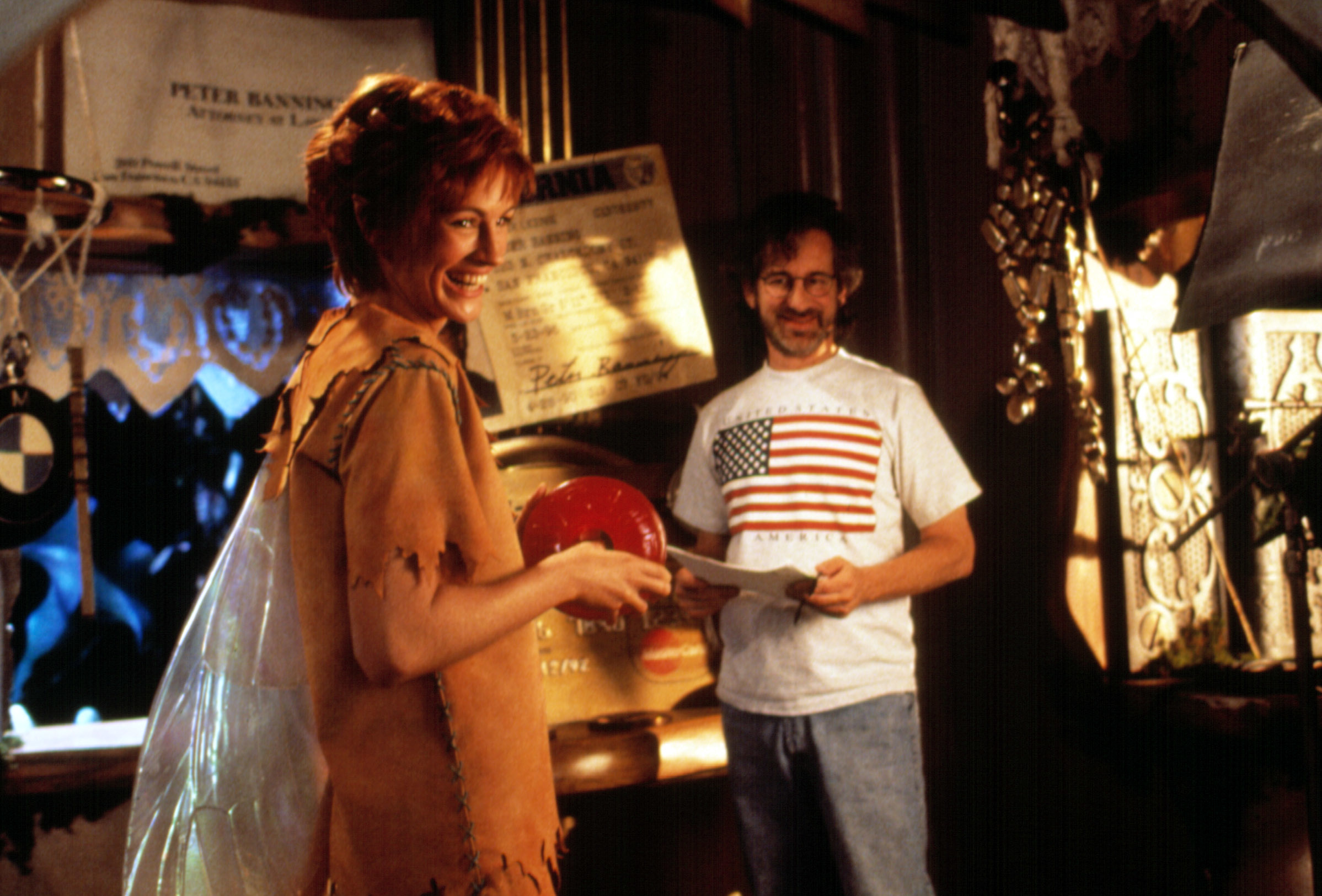 Julia Roberts in a pixie costume and Steven Spielberg on a movie set, with Roberts holding a prop and Spielberg smiling