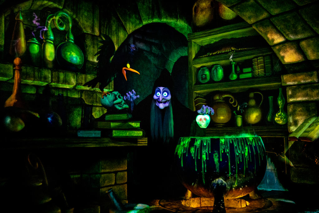 Animated scene featuring an old witch in a dark dungeon, holding a glowing skull over a bubbling cauldron amid shelves filled with potions and ingredients