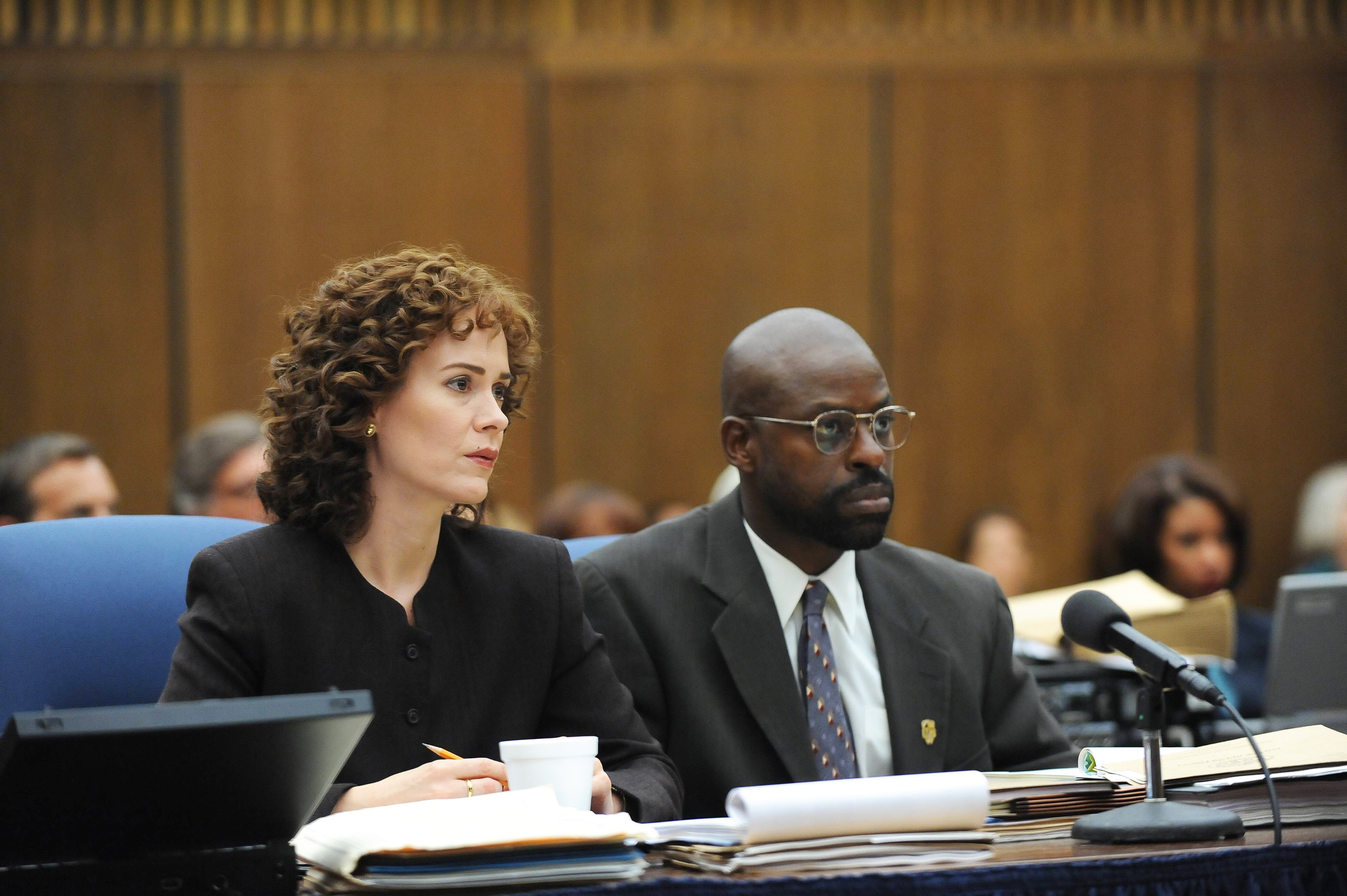 Sarah Paulson and Sterling K. Brown in a courtroom scene, both dressed in formal business attire with serious expressions