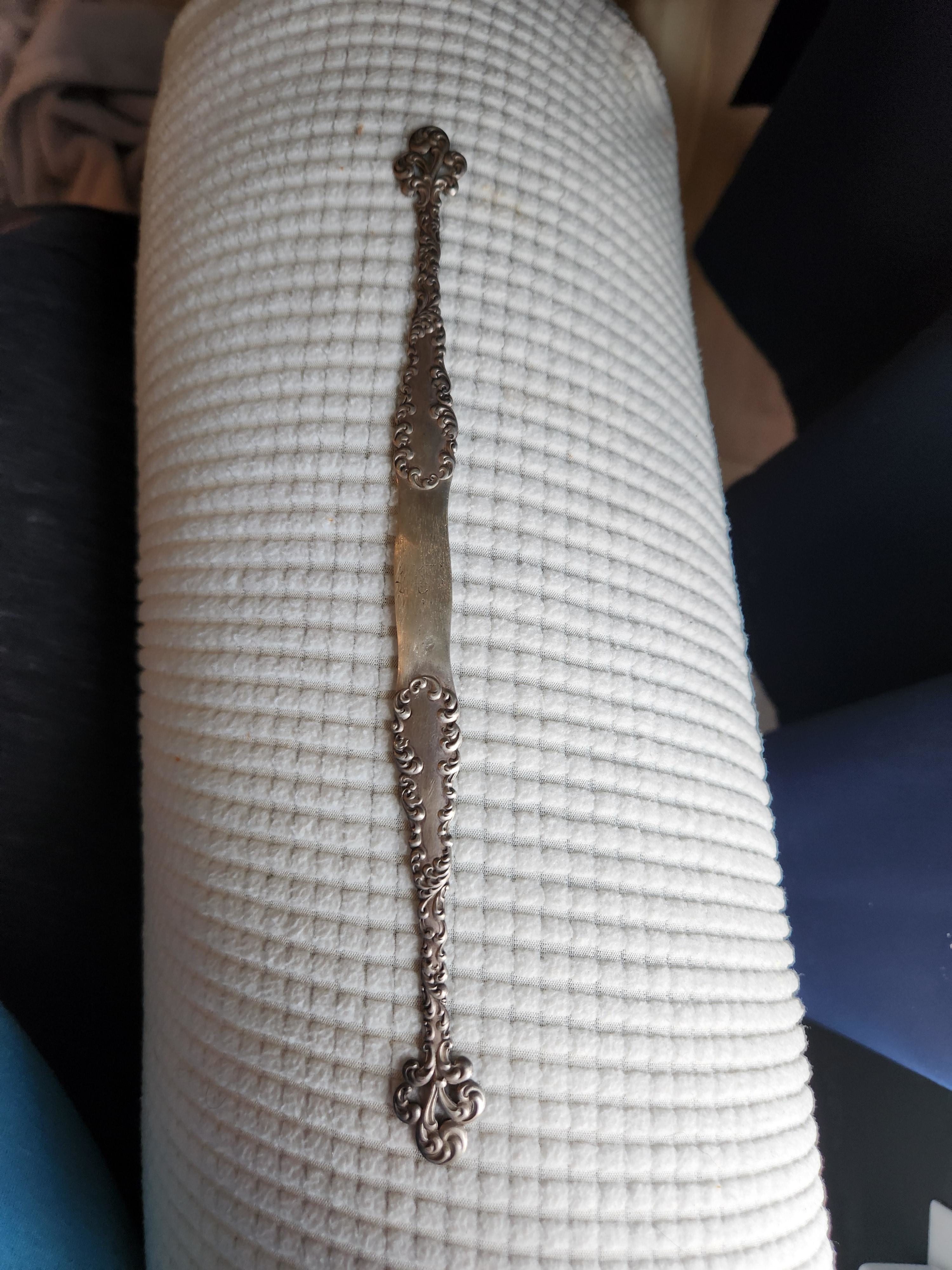 A decorative metal stick with intricate carvings on both ends is placed on a textured white surface