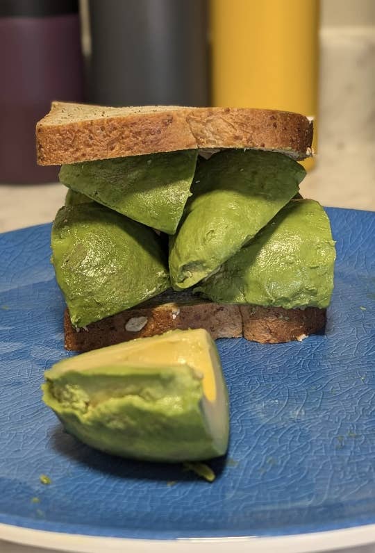 A sandwich made of sliced avocado on bread, placed on a blue plate