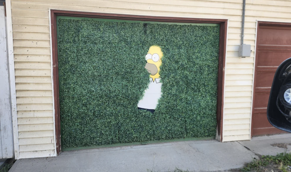 Garage door features a mural of Homer Simpson partially disappearing into hedge