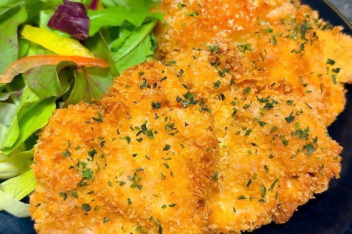 サクサクのカツレツと新鮮なグリーンサラダが黒い皿に盛り付けられています。