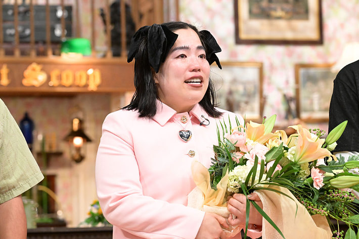 お名前がわからない女性が、涙を流しながら花束を抱えています。彼女はピンクの服を着ています。