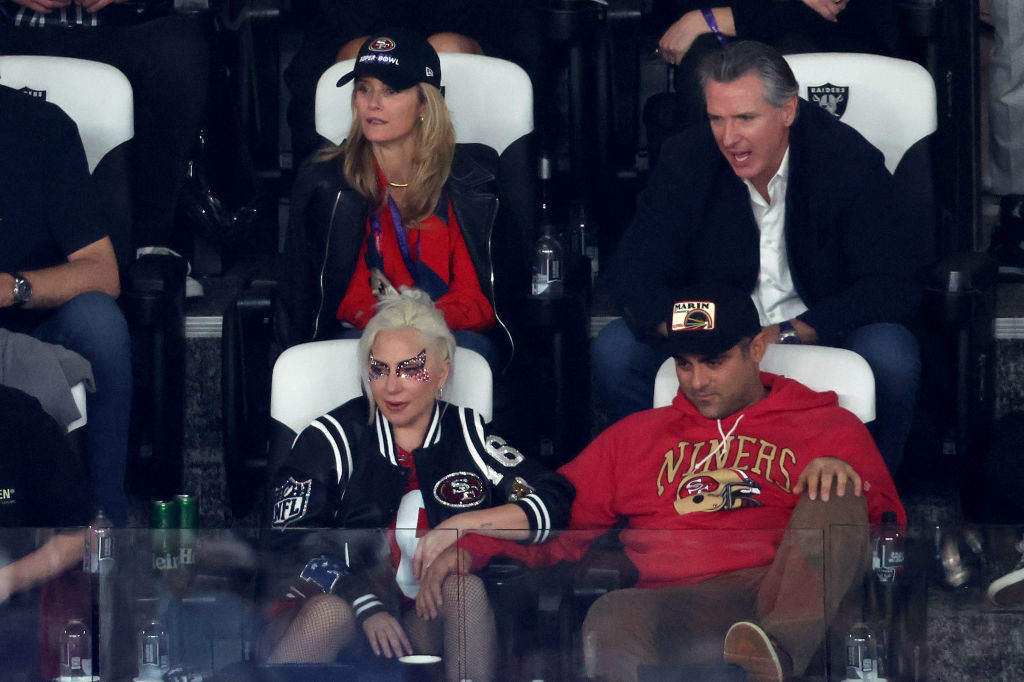 Lady Gaga, Christian Carino, and Jennifer Newsom attend a sports event. Lady Gaga wears a sequined mask and a 49ers jacket